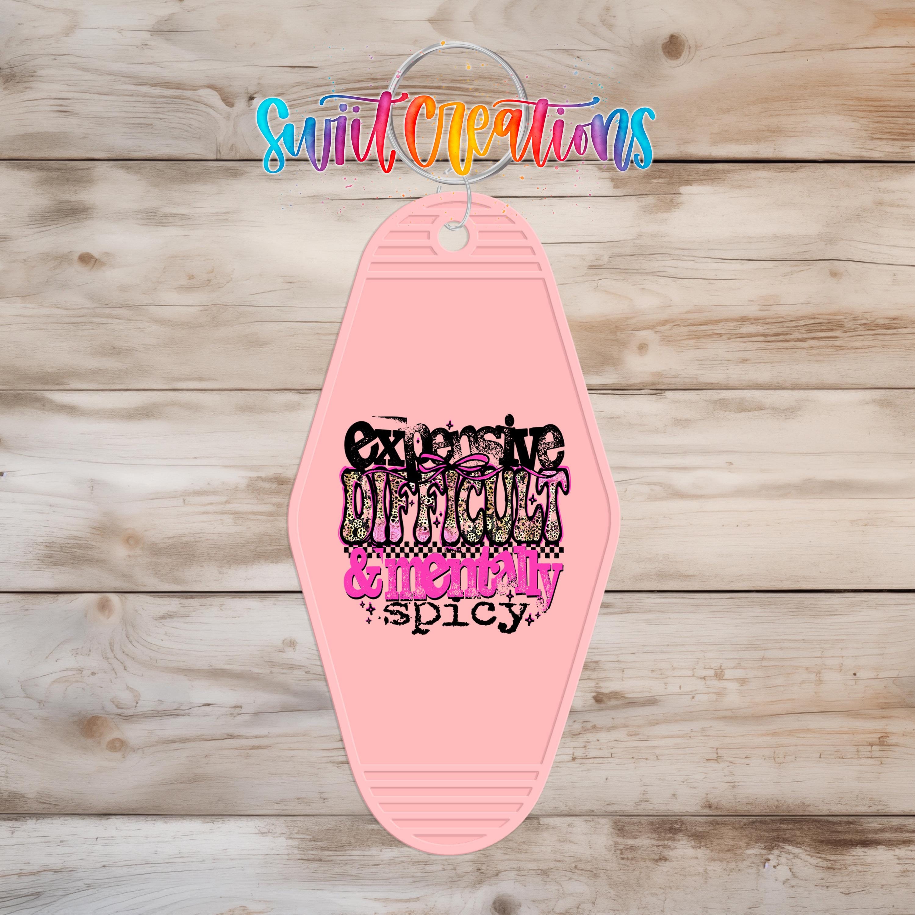 A pink keychain with a colorful, stylized text design on it, hanging on a wooden surface.