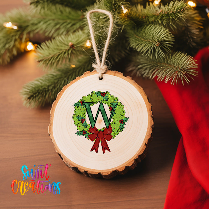 A round wooden ornament with a letter "W" and a holly wreath design hangs on a Christmas tree.