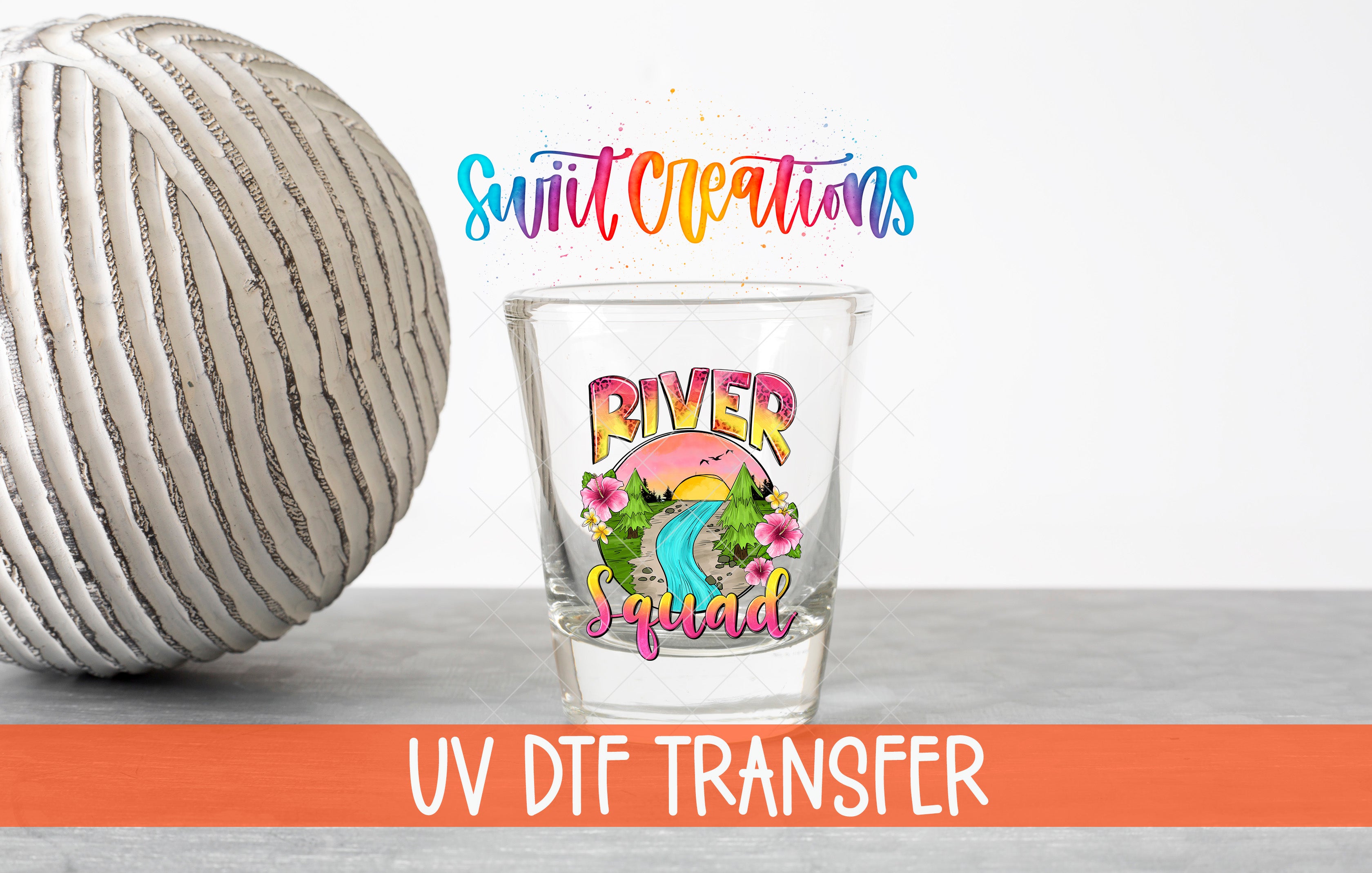 a glass with a colorful design and text, placed next to a gray ball on a gray surface.