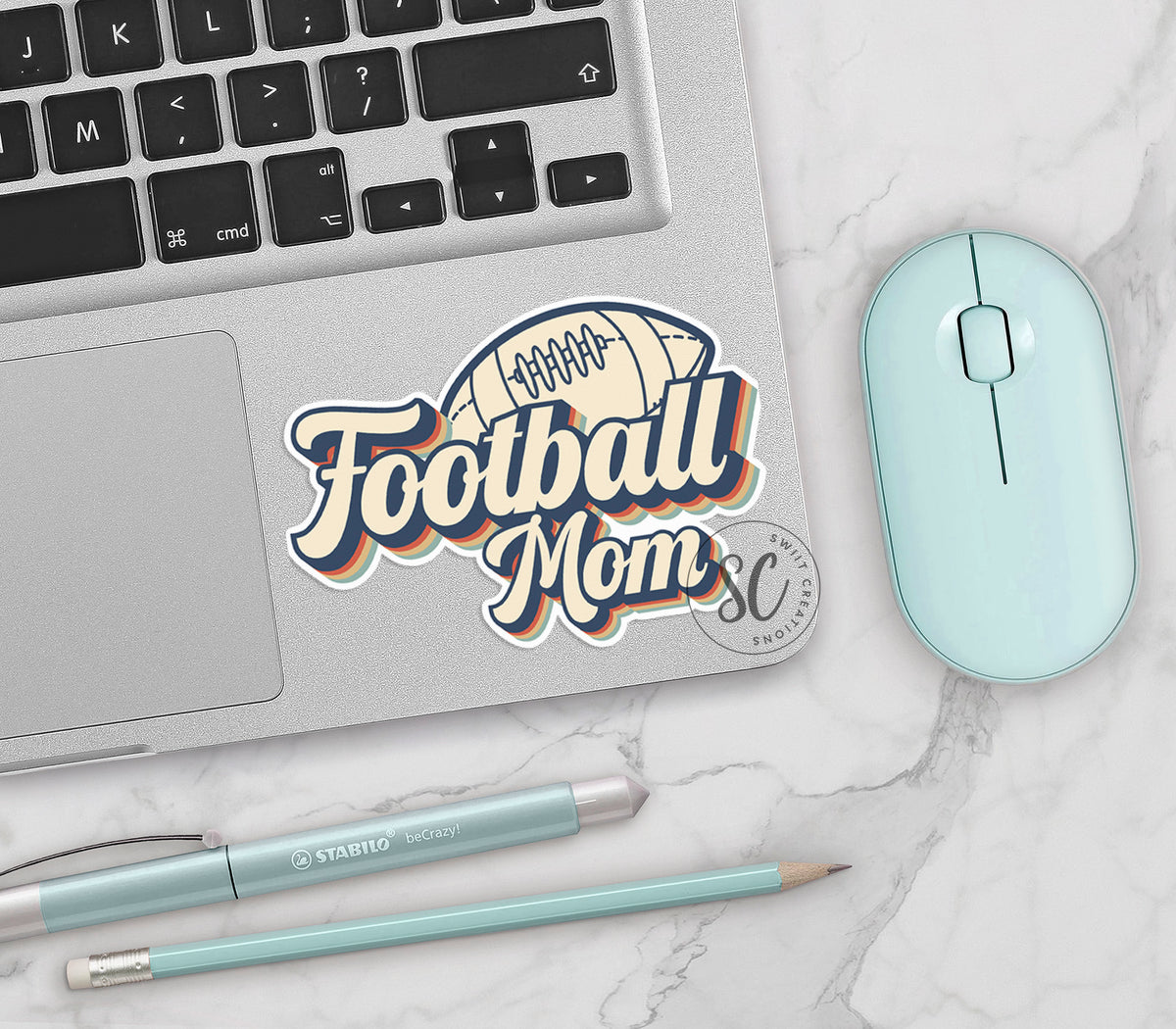 Football Mom vinyl sticker on a silver laptop next to a mint mouse and pens