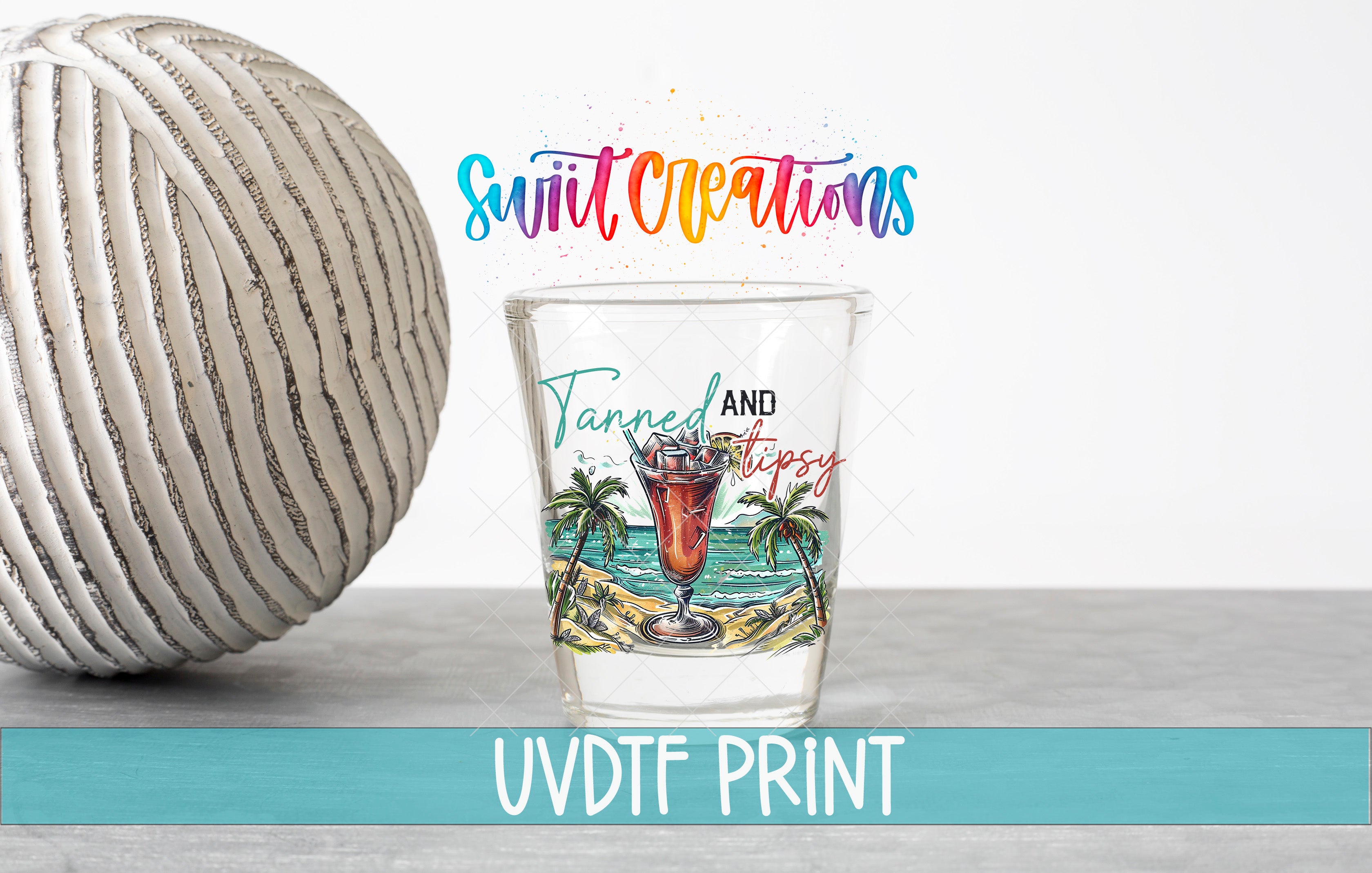 a shot glass with a tropical beach scene and palm trees, along with the text "Swift Creations" and "Tanned and Tipsy" printed on it.