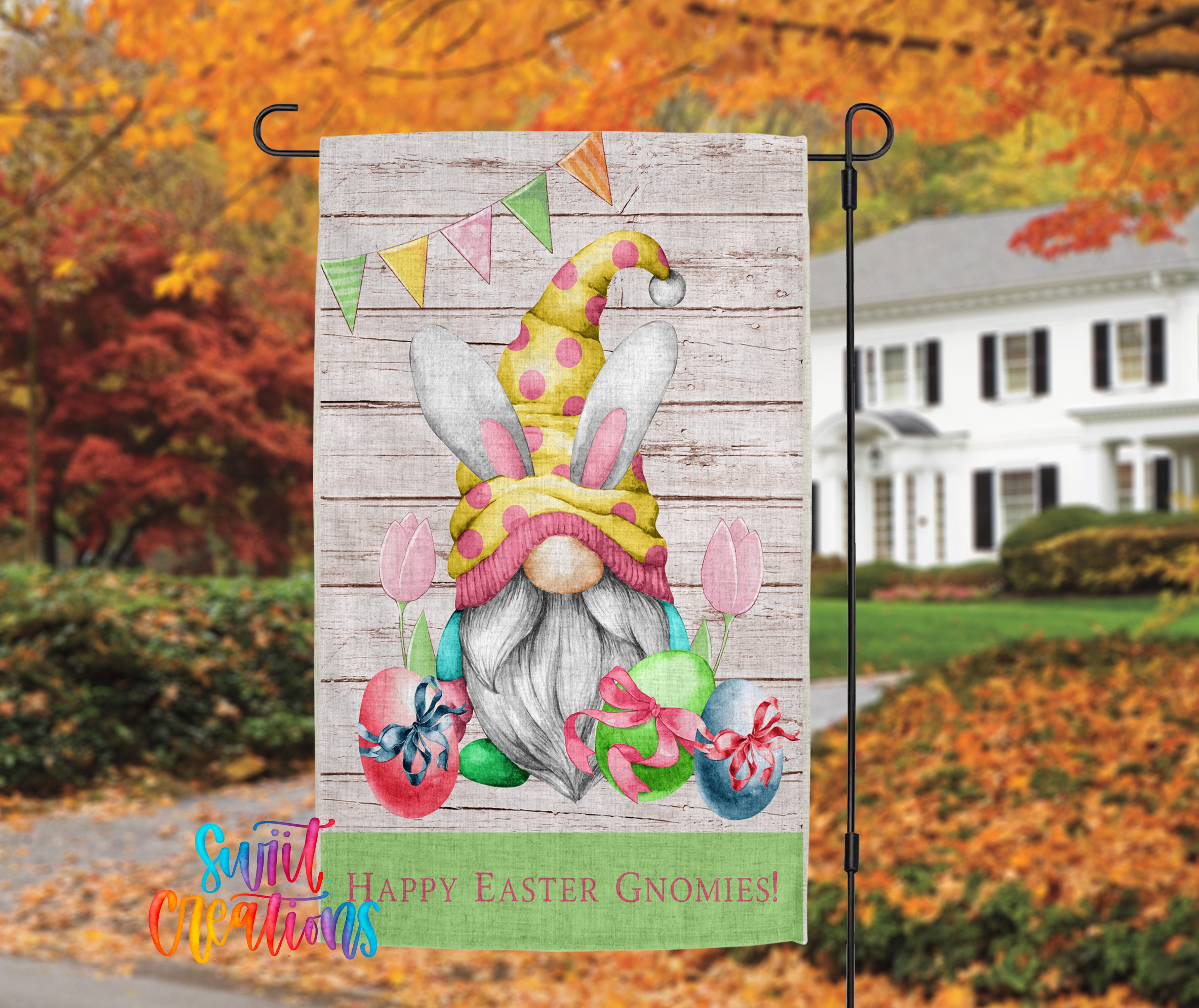 A colorful Easter-themed garden decoration featuring a gnome holding a basket of eggs and flowers, with a house and autumn foliage in the background.