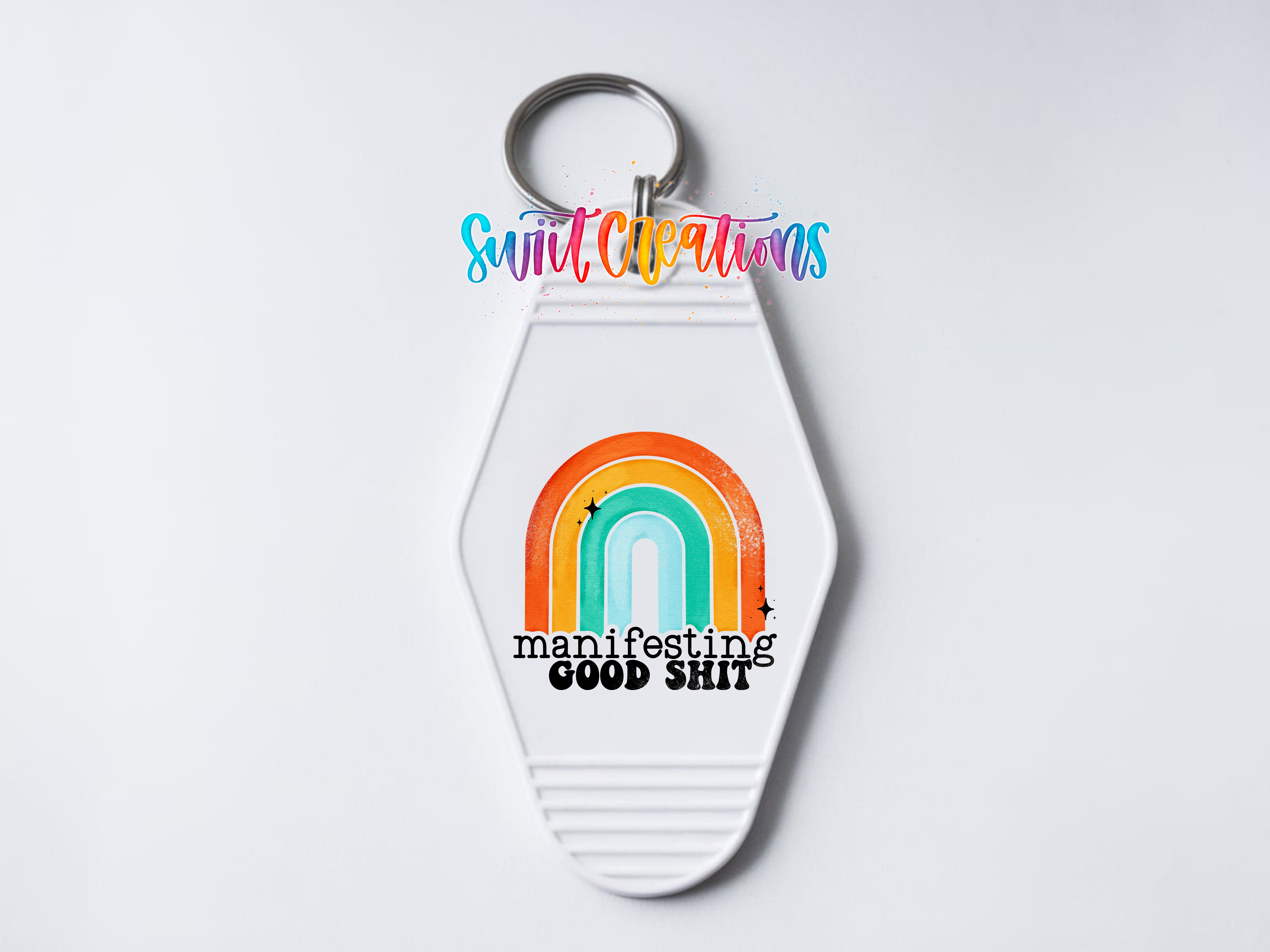 A keychain with a colorful rainbow graphic and the text "manifesting good shit" printed on it.