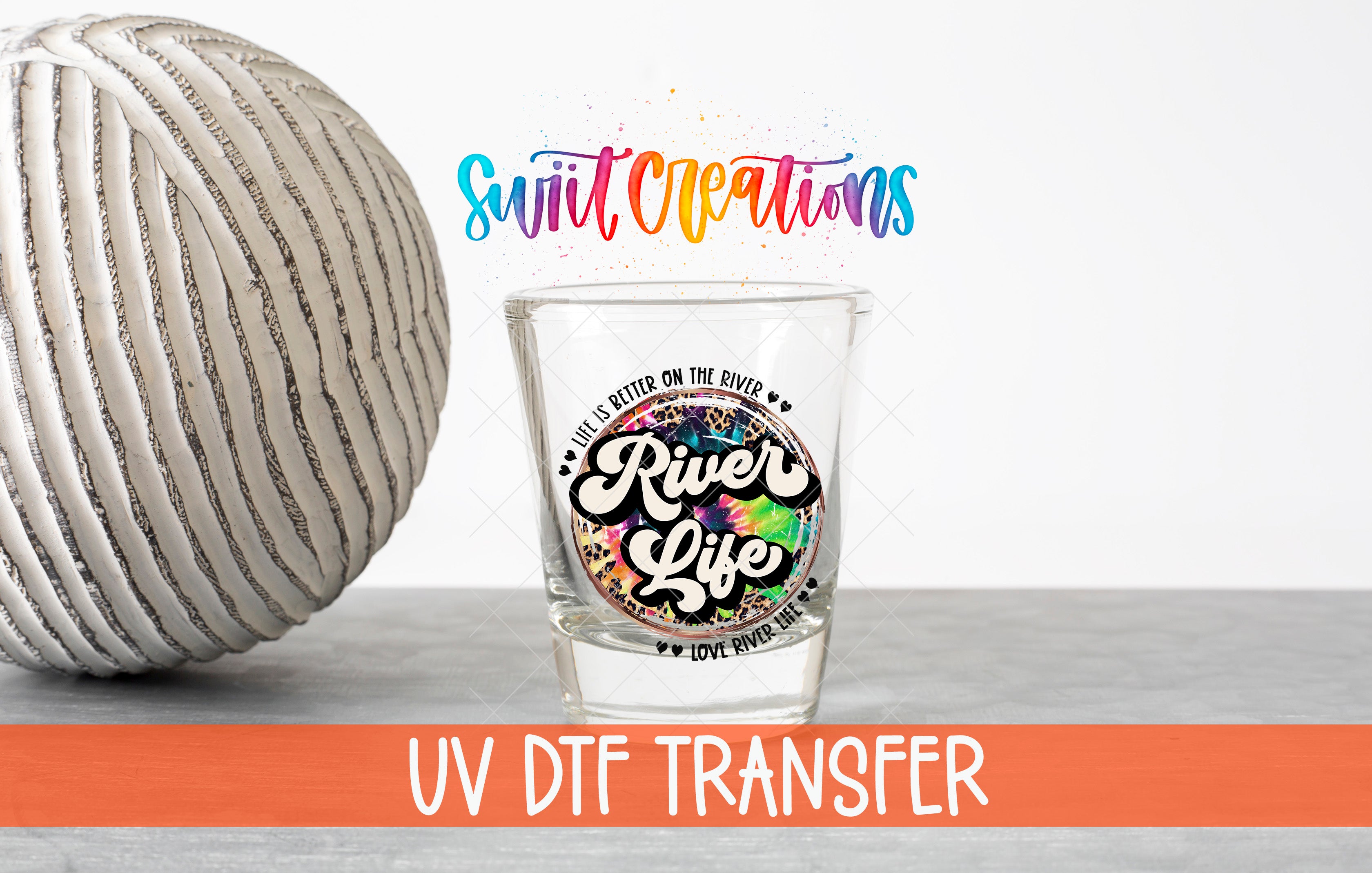 a shot glass with a colorful design and text, placed next to a white ball on a gray surface.