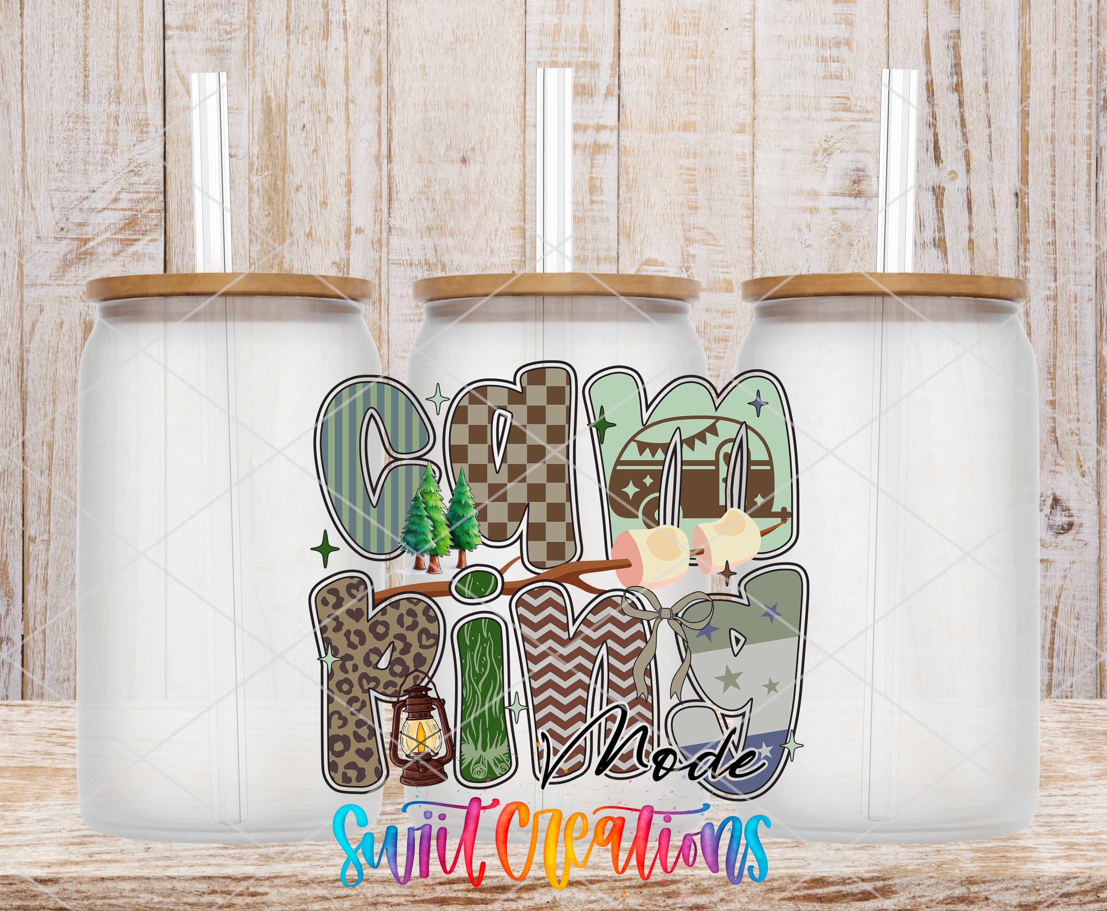three glass jars with lids, each containing a straw, arranged in a row against a wooden background. The jars are decorated with various text and illustrations, including the word "Camping" and other decorative elements.