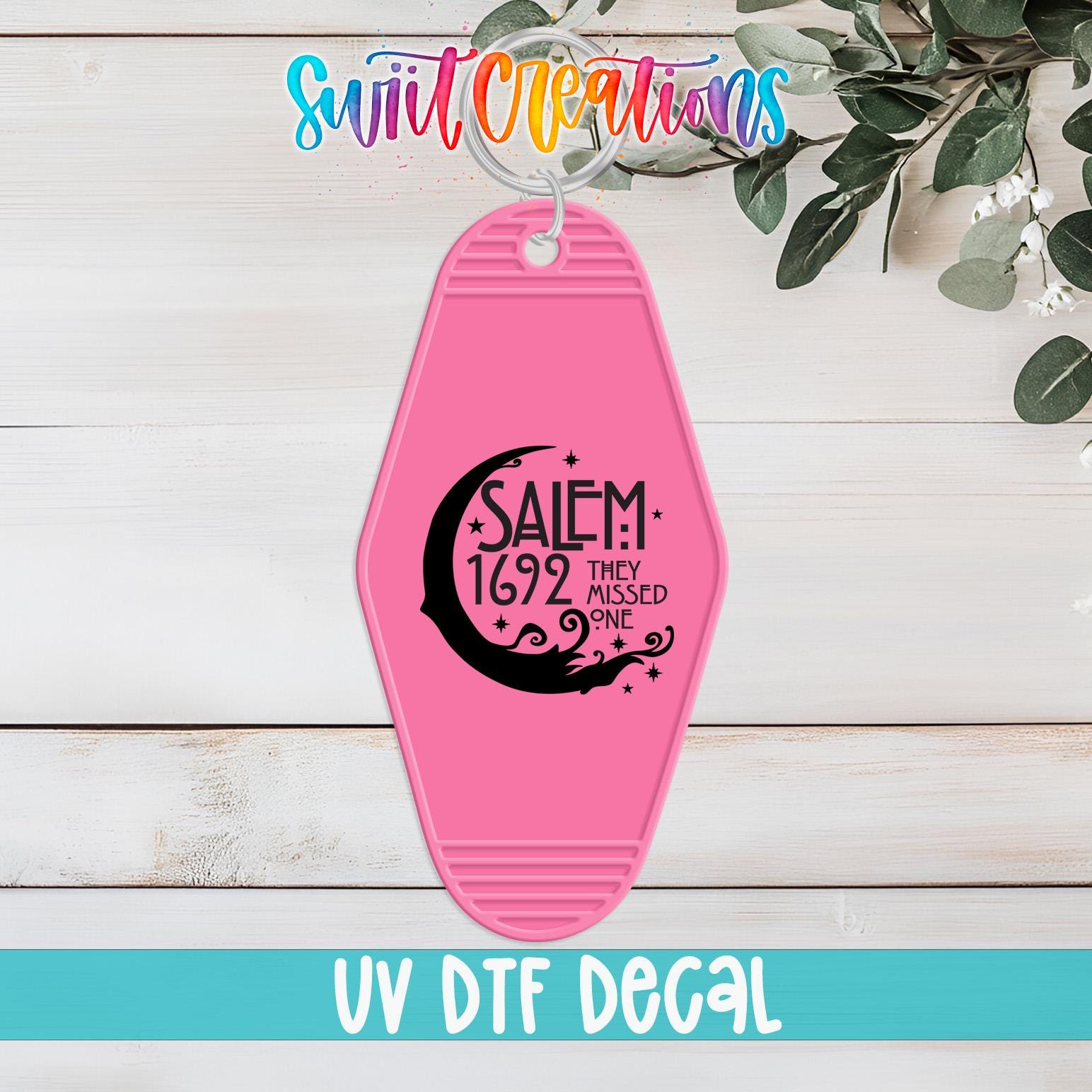 A pink keychain with a black and white design and text, placed on a white wooden surface.