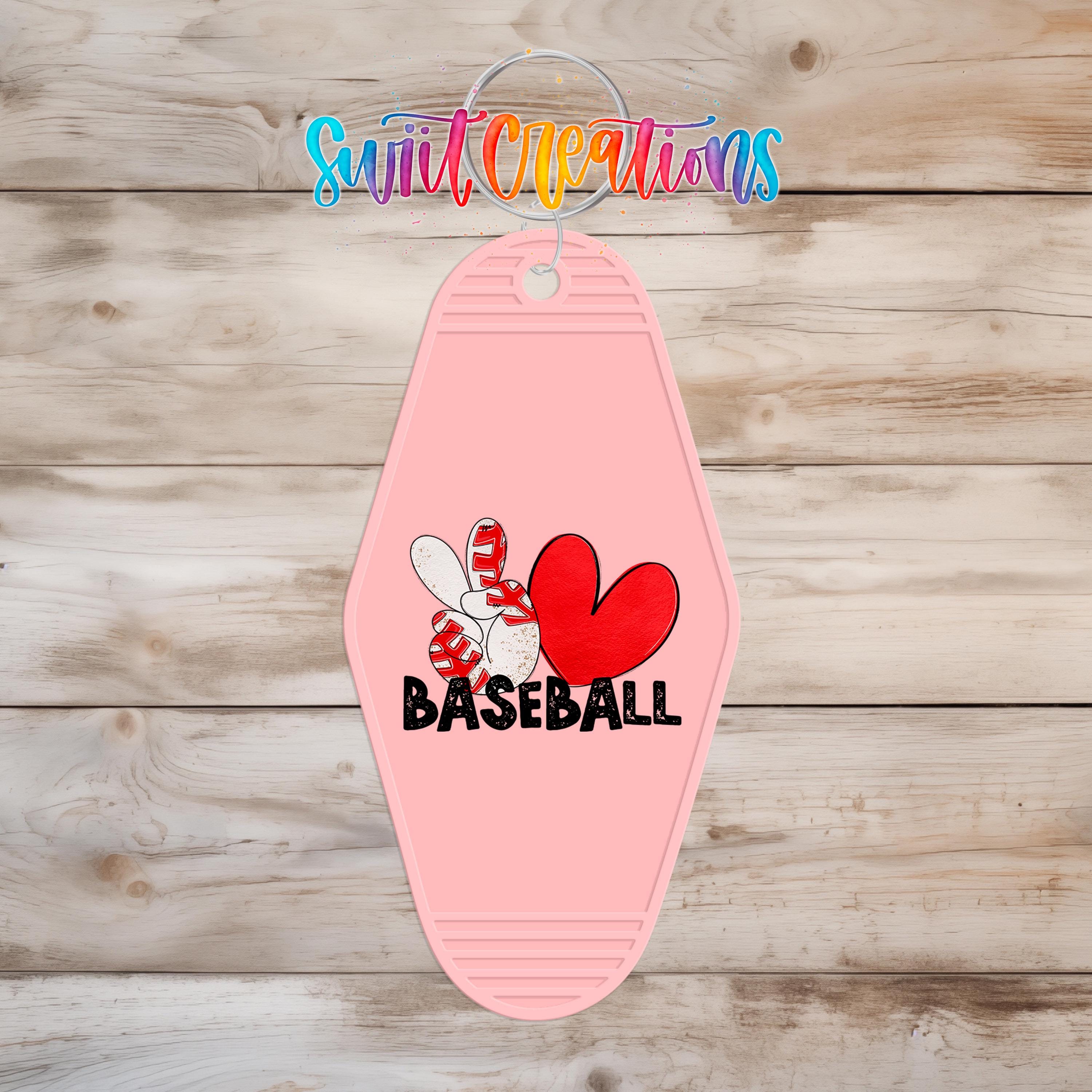 A pink keychain with a baseball graphic and the word "BASEBALL" printed on it, hanging on a wooden surface.