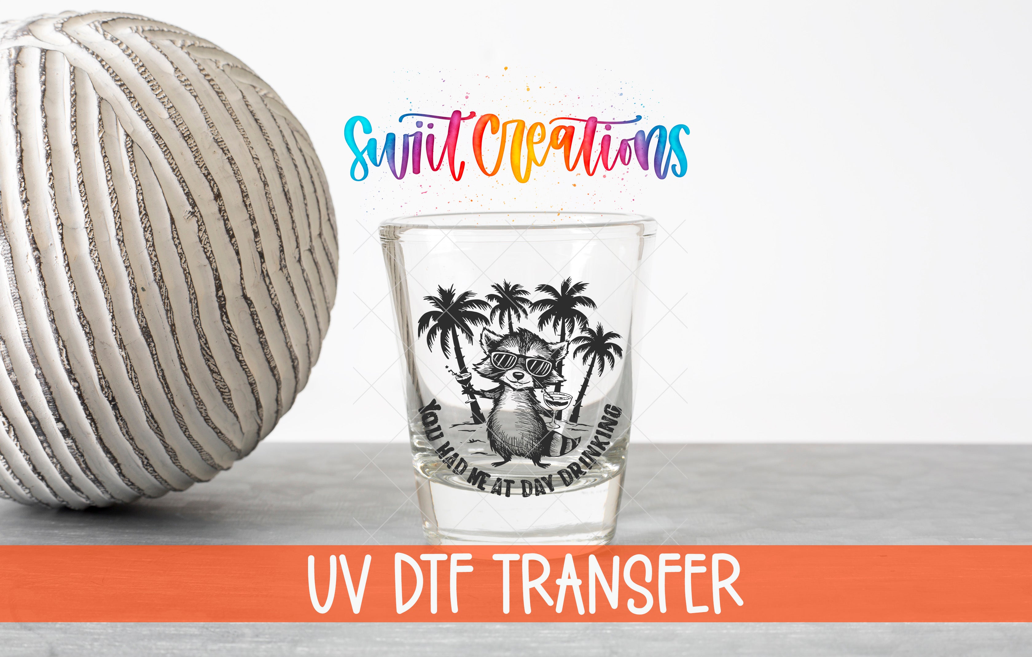 a shot glass with a graphic design and text, placed next to a striped ball and a text overlay that says "Swit Creations UV Dtf Transfer".