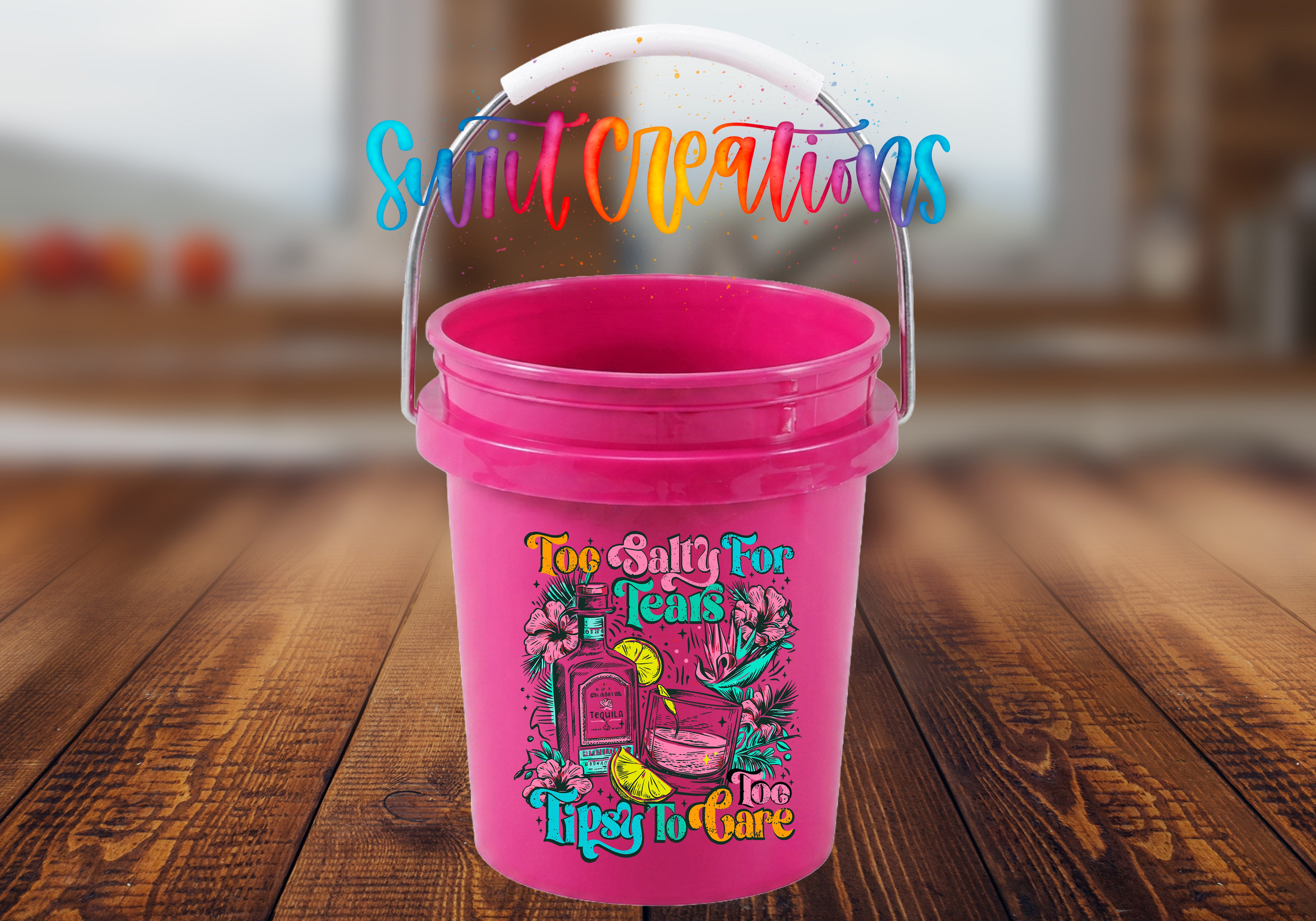 A pink bucket with a colorful graphic and text printed on it, placed on a wooden surface.