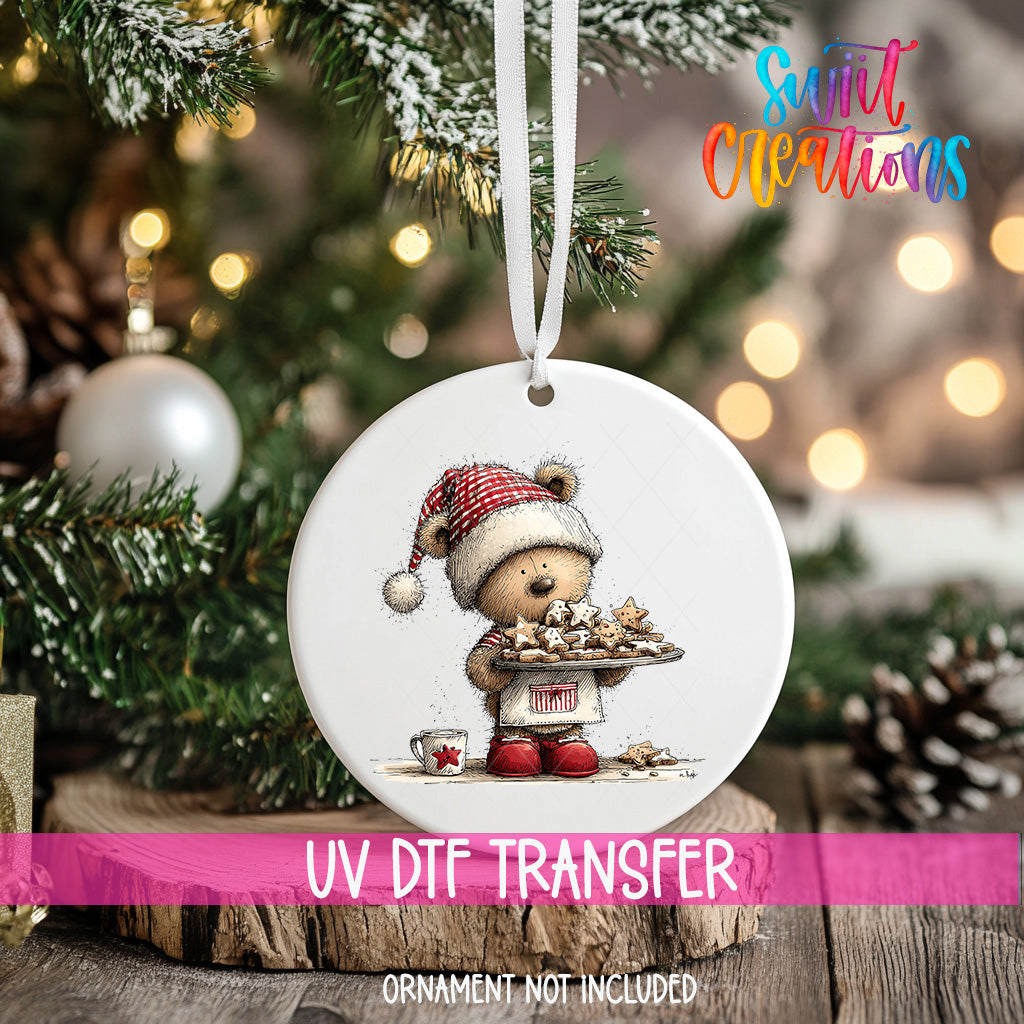 A white ornament with a teddy bear wearing a Santa hat and holding a tray of cookies, hanging on a Christmas tree.