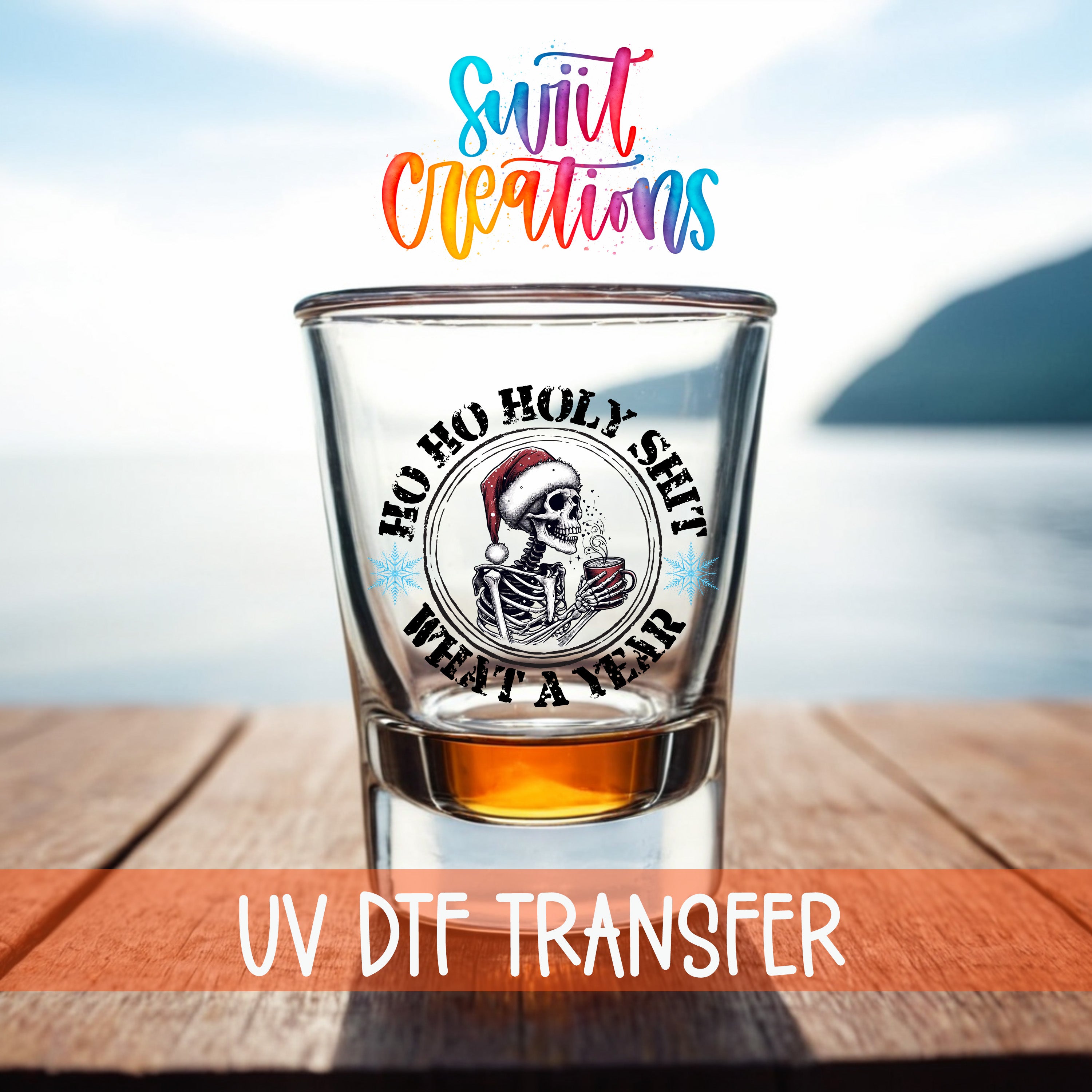 A shot glass with a skull wearing a Santa hat and holding a mug, set against a blurred background of a body of water and a mountain.