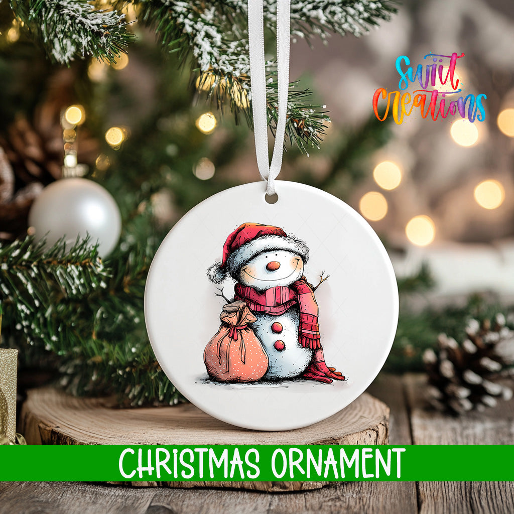 A white Christmas ornament featuring a snowman is hanging from a tree branch, with a blurred background of pine branches and twinkling lights.