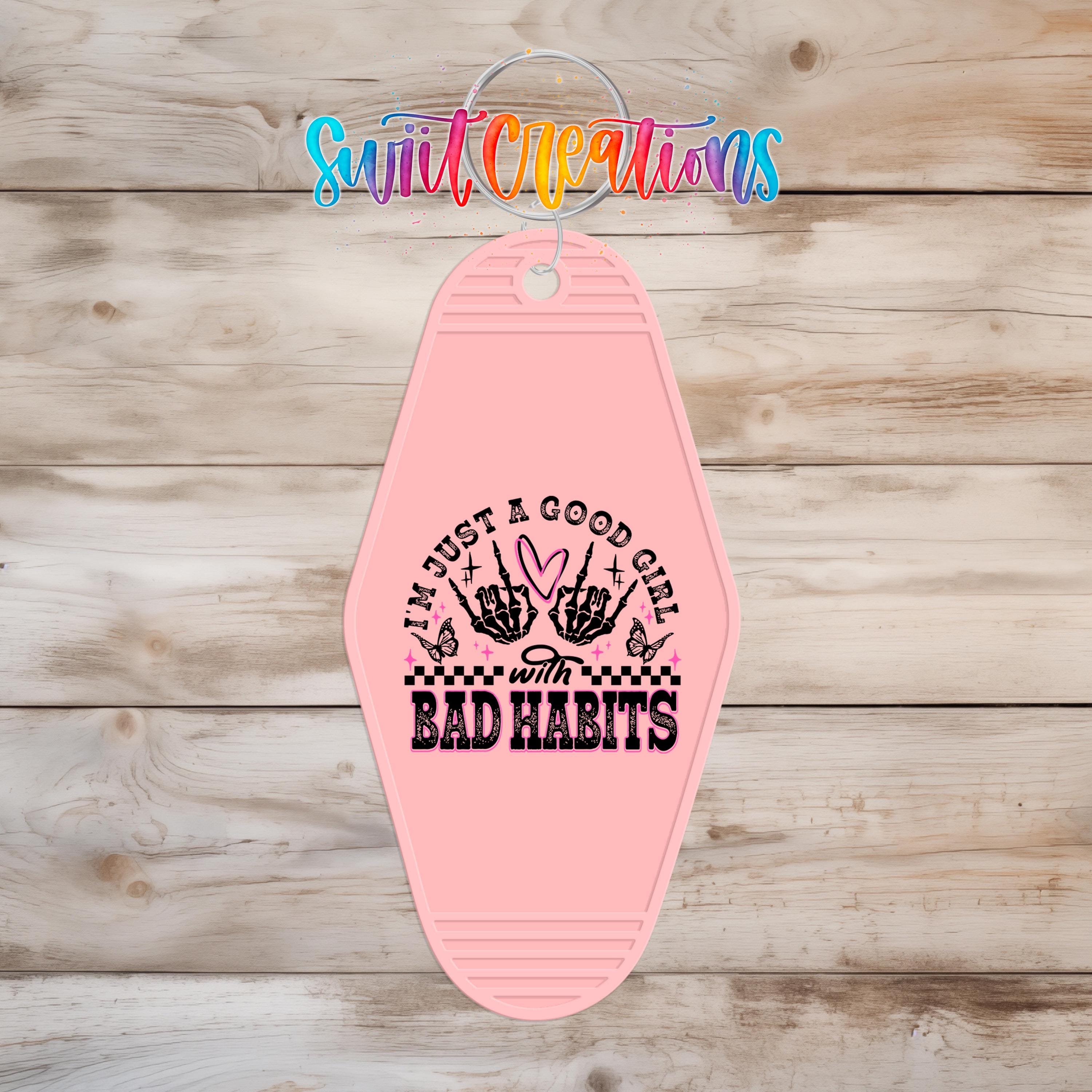 A pink keychain with a graphic design and text on it, hanging on a wooden surface.