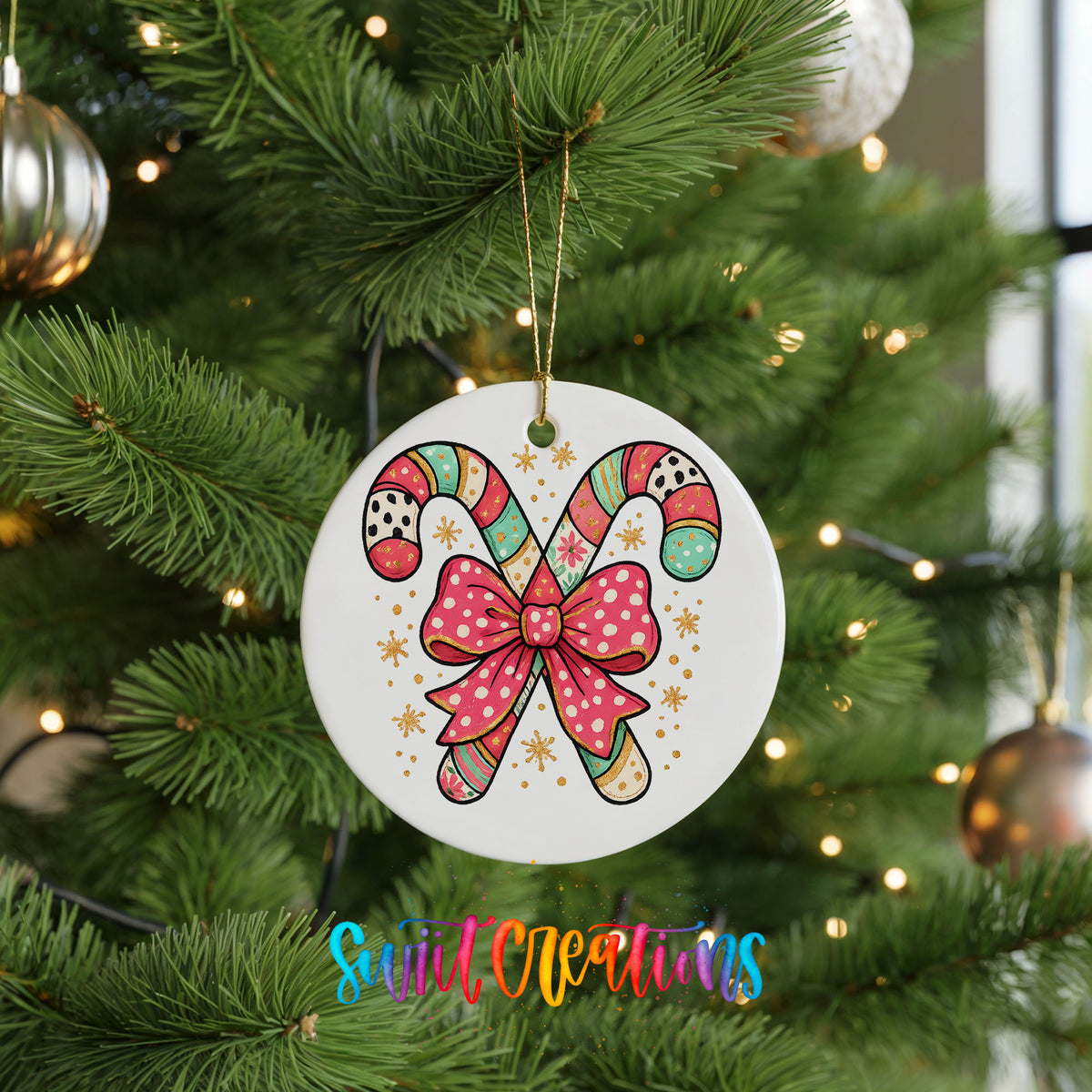 A white ornament with a candy cane design and a pink bow is hanging on a Christmas tree.