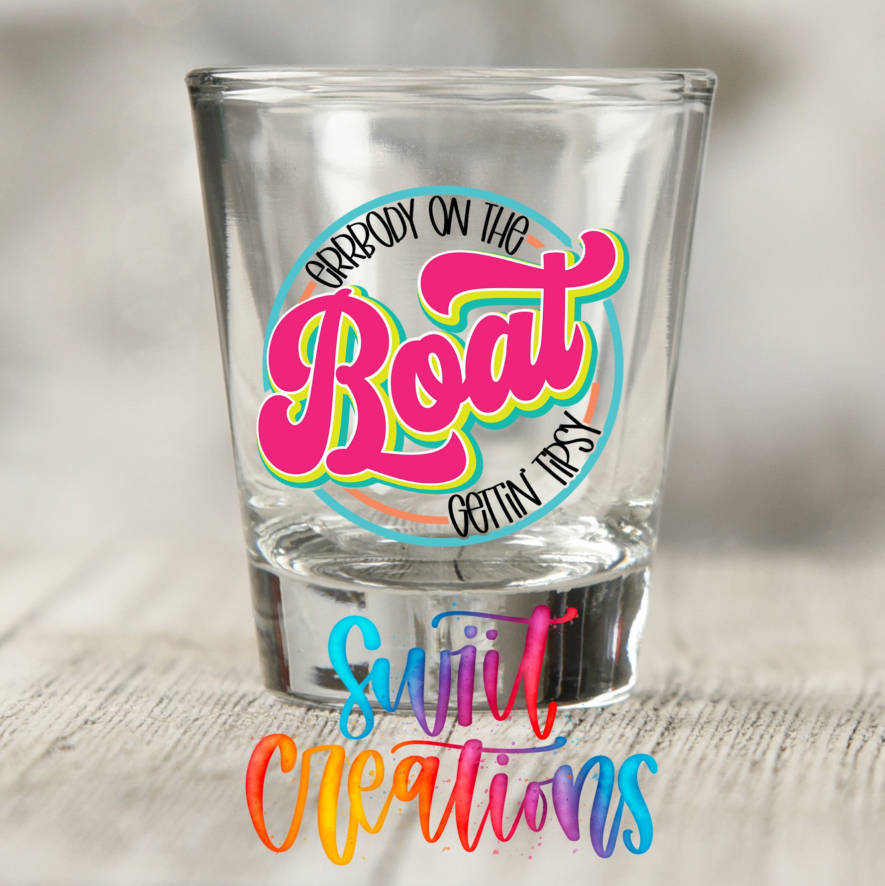 A shot glass with a colorful, stylized text design on it, placed on a wooden surface.