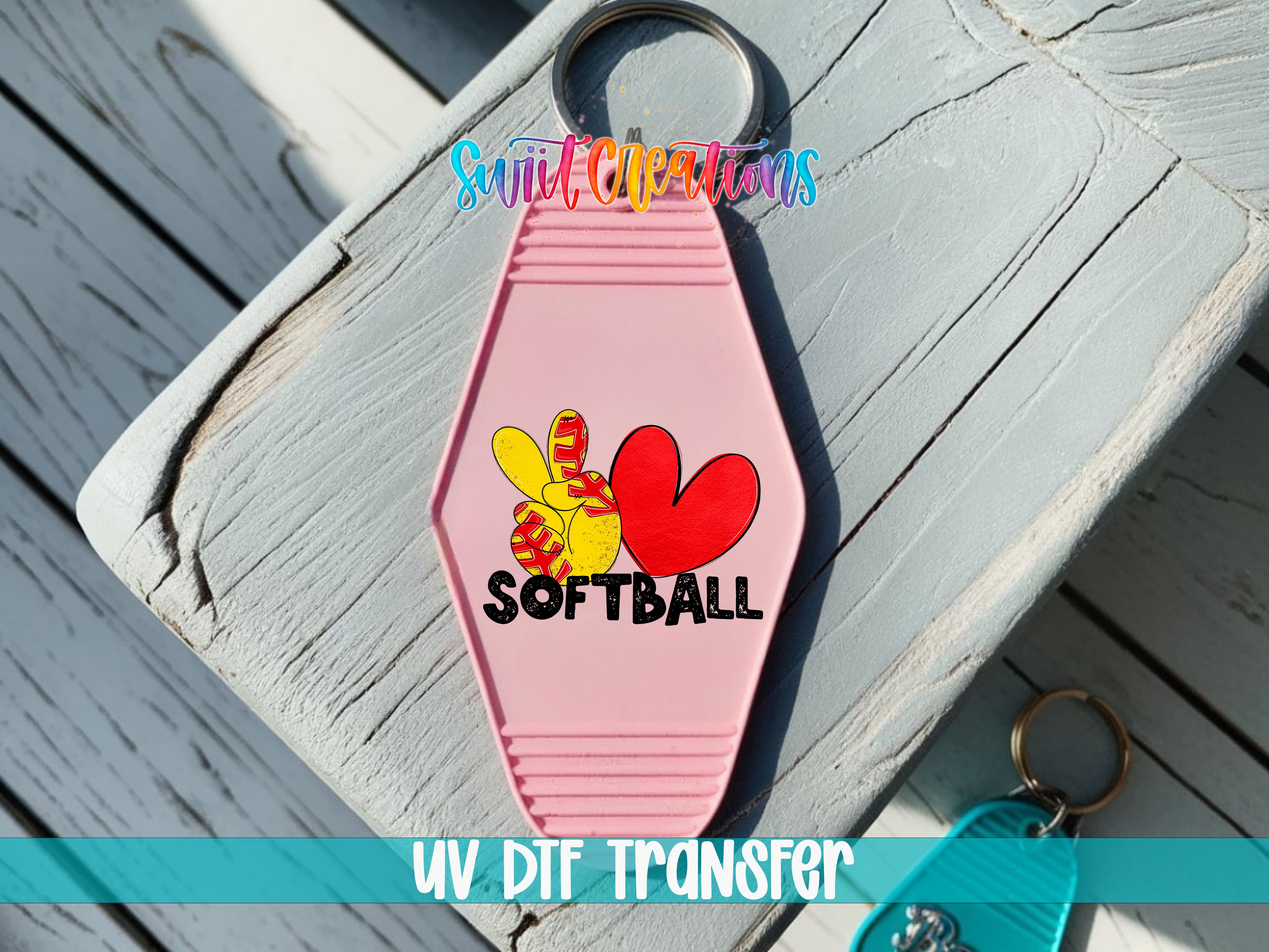 A pink keychain with a heart and softball design, placed on a wooden surface.