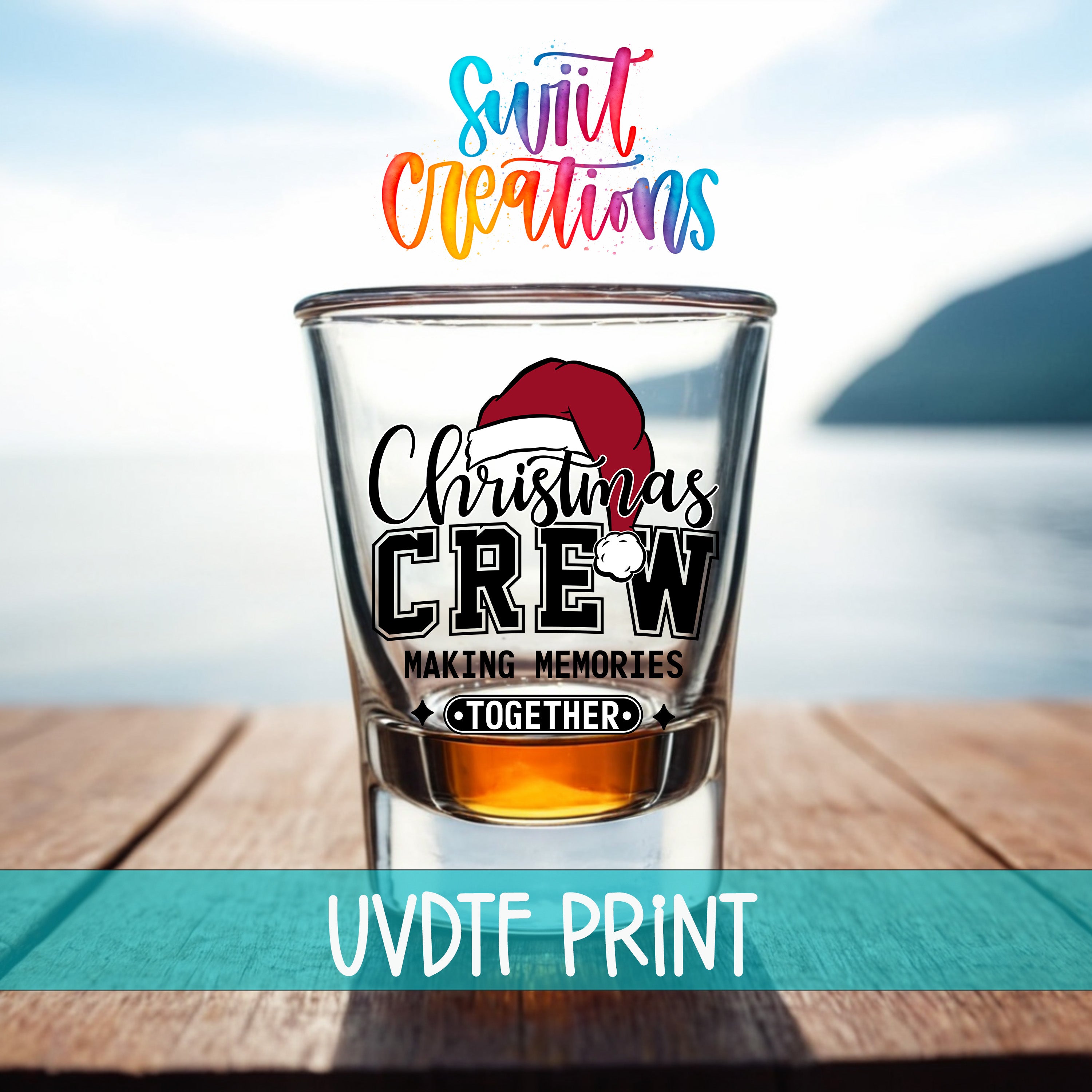 A shot glass with a Christmas crew design on it, placed on a wooden surface with a body of water in the background.