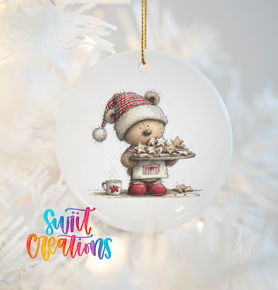 A white oval ornament featuring a teddy bear wearing a red and white striped hat, holding a tray of cookies, and standing on a white surface.
