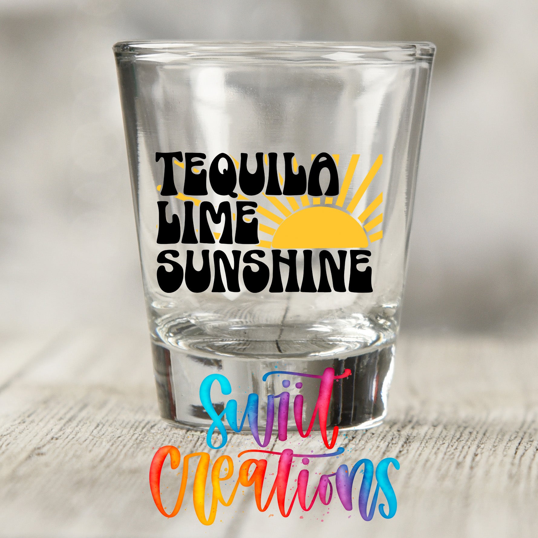 A clear shot glass with the text "Tequila Lime Sunshine" printed on it, along with a colorful graphic design.