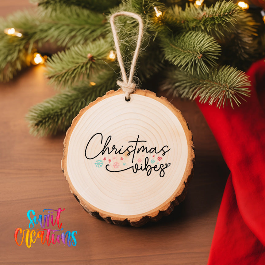A wooden ornament with the text "Christmas vibes" hanging from a tree branch, surrounded by pine branches and twinkling lights.