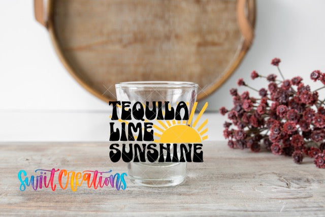 A glass with the text "Tequila Lime Sunshine" on it, placed on a wooden surface next to a bunch of red flowers.