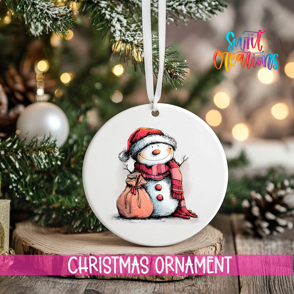 A white Christmas ornament featuring a snowman is hanging from a tree branch, with a blurred background of lights and greenery.