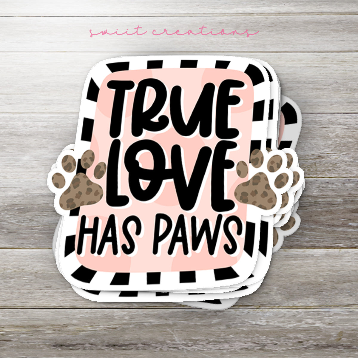 Stack of True Love Has Paws glossy stickers on a gray wood table