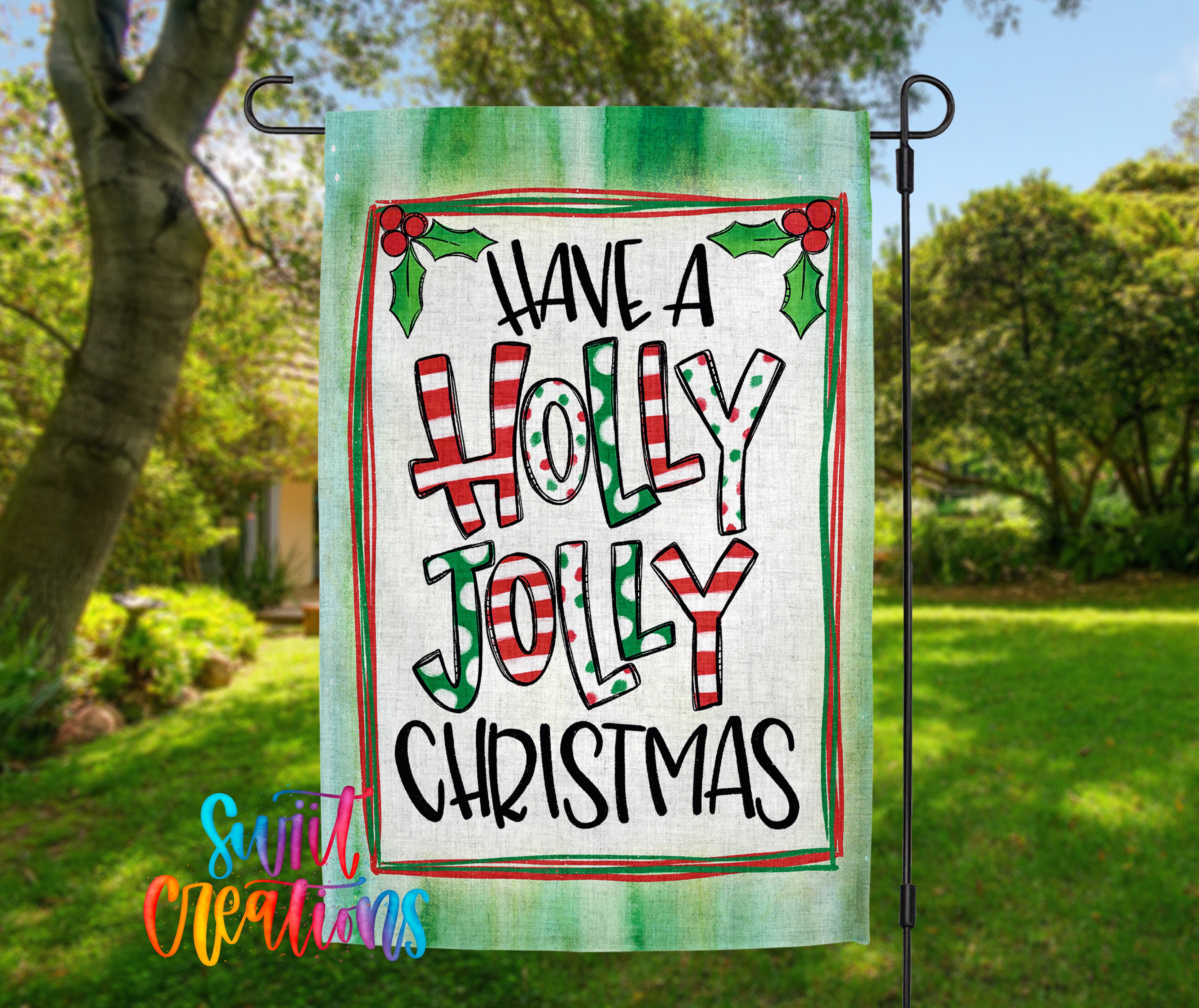 A green and white flag with the text "Have a HOLY JOYL Christmas" displayed on it, hanging in a garden setting with trees and greenery in the background.