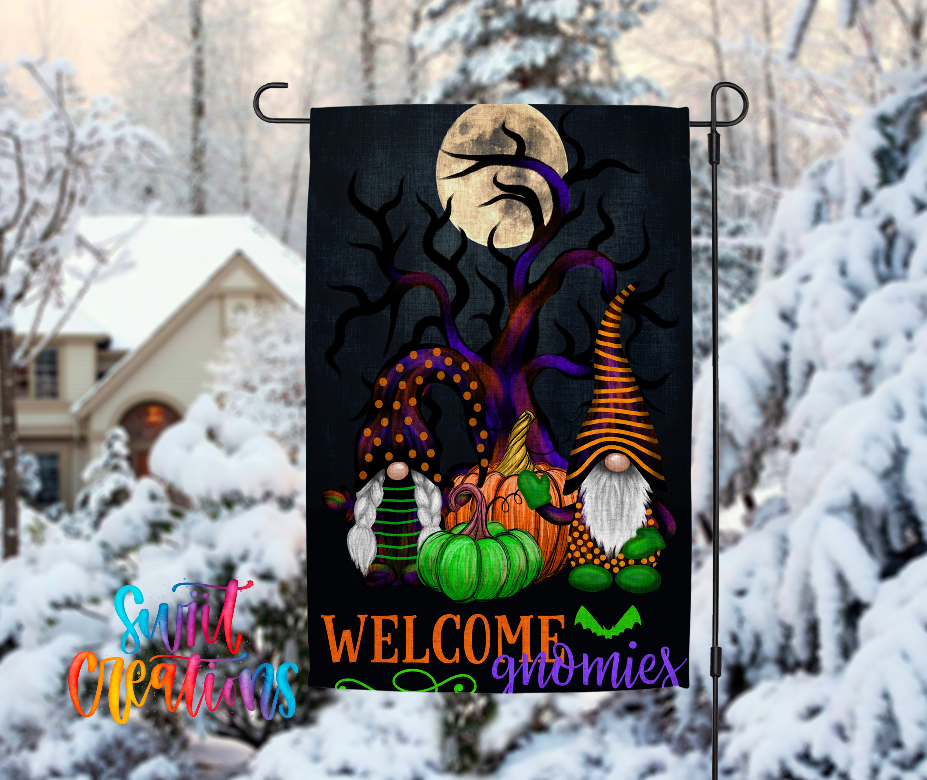A Halloween-themed garden flag featuring gnomes and pumpkins, with a full moon in the background, is displayed in a snowy outdoor setting.