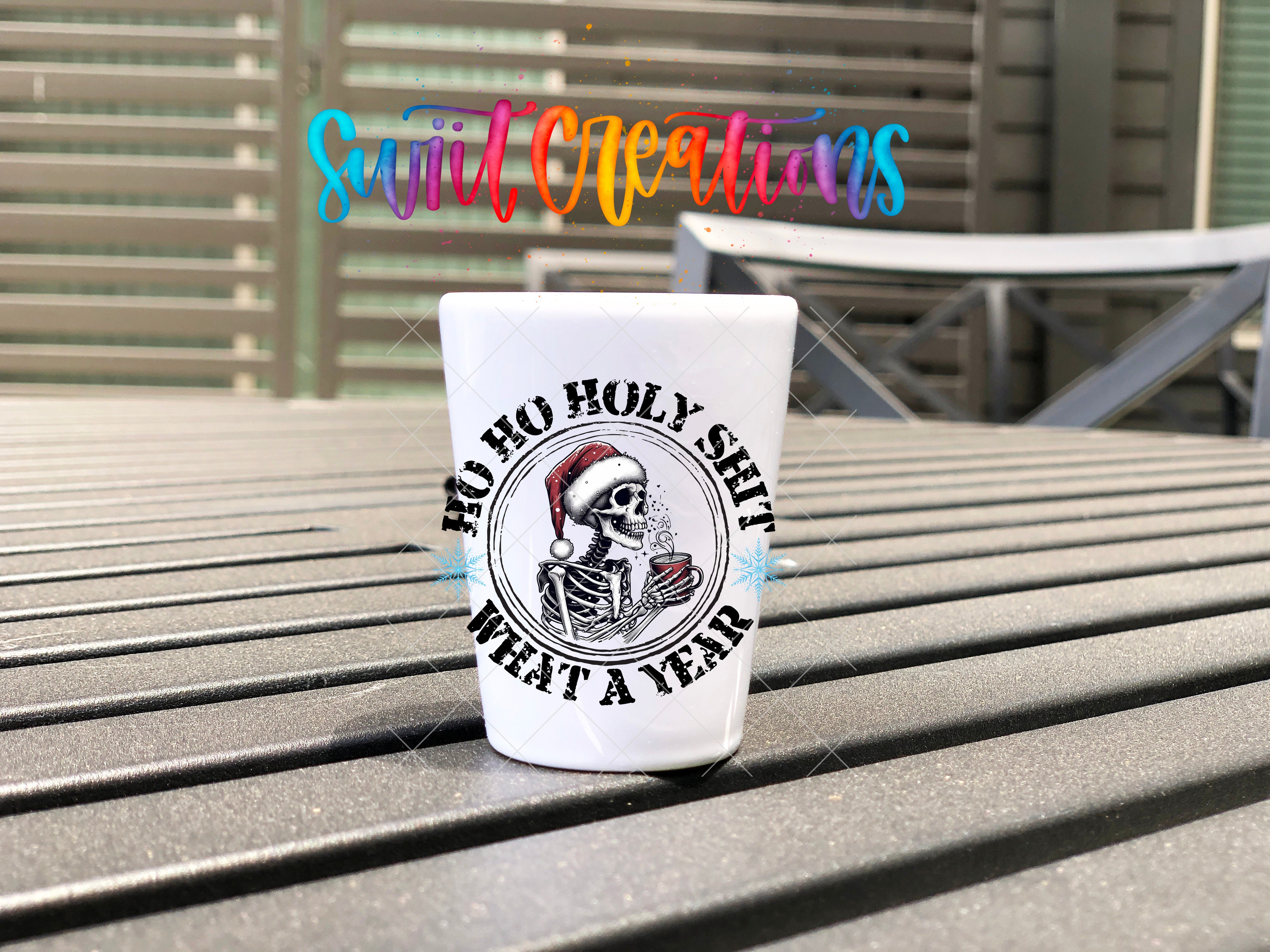 A white shot glass with a graphic design and text on it, placed on a wooden surface.