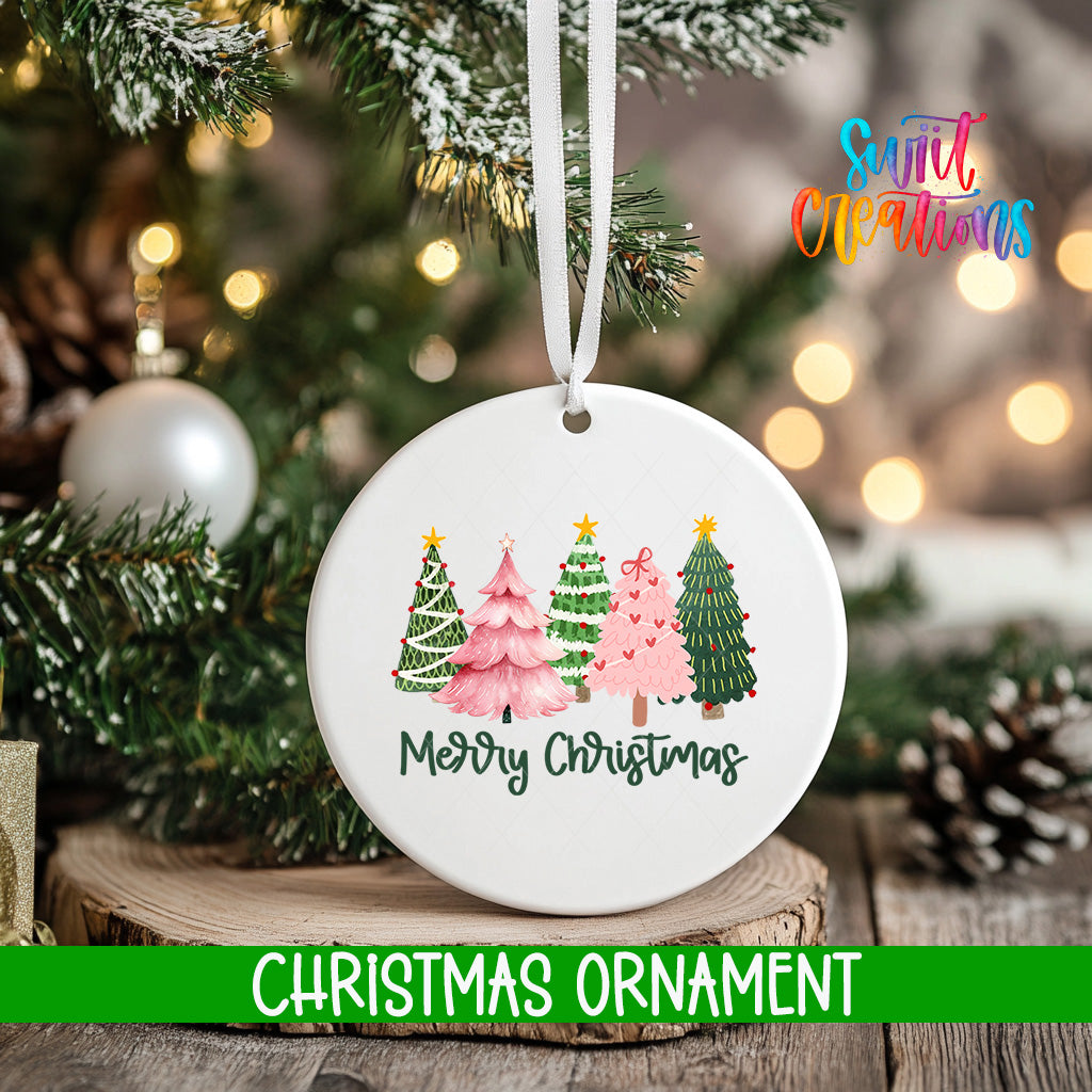 A white Christmas ornament with a design of four different colored Christmas trees, hanging on a tree branch.