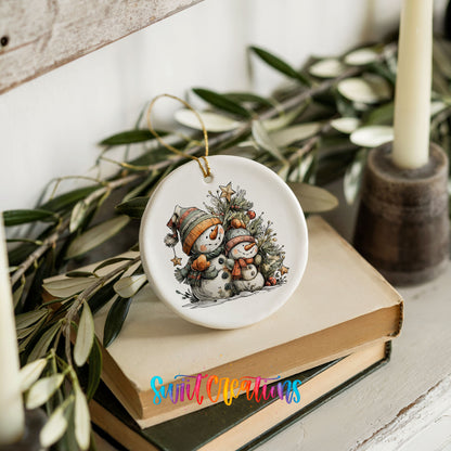 A ceramic ornament featuring two snowmen is displayed on top of a stack of books, surrounded by greenery.