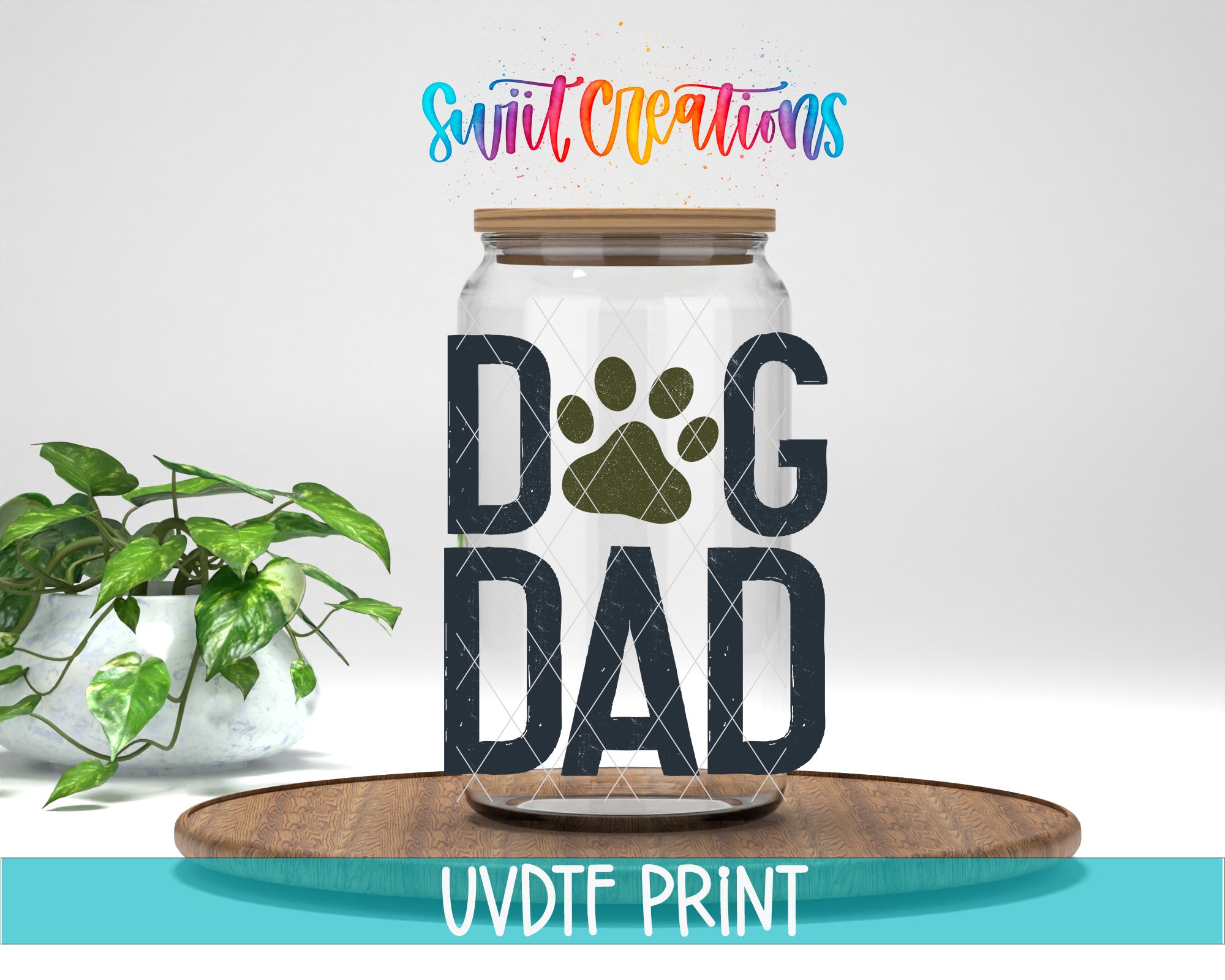 A glass jar with a paw print design and the text "DOG DAD" inside it, placed on a wooden surface. There is also a potted plant in the background.