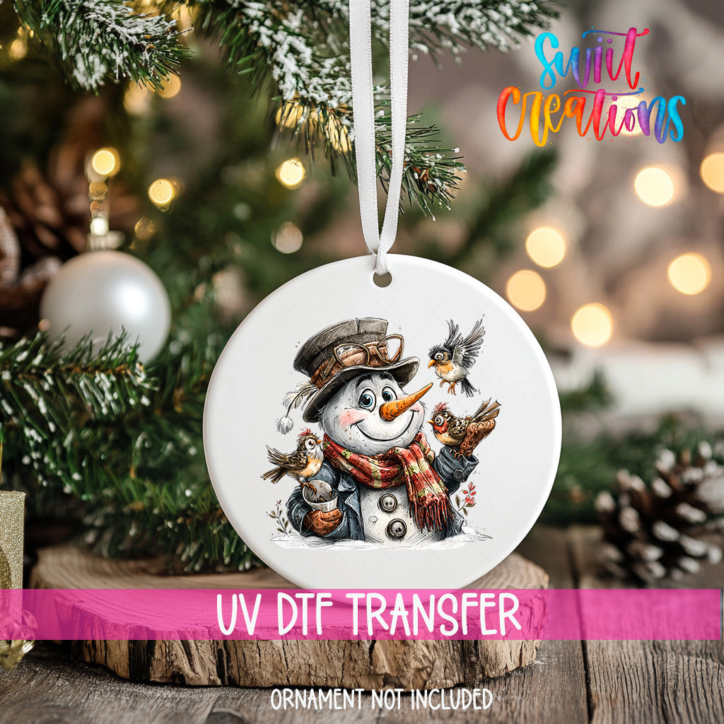 A white ornament with a snowman and birds hanging from it, placed on a Christmas tree.