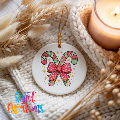 A white ceramic ornament with a colorful candy cane design and a pink bow, placed on a white knitted blanket with dried flowers and a lit candle nearby.