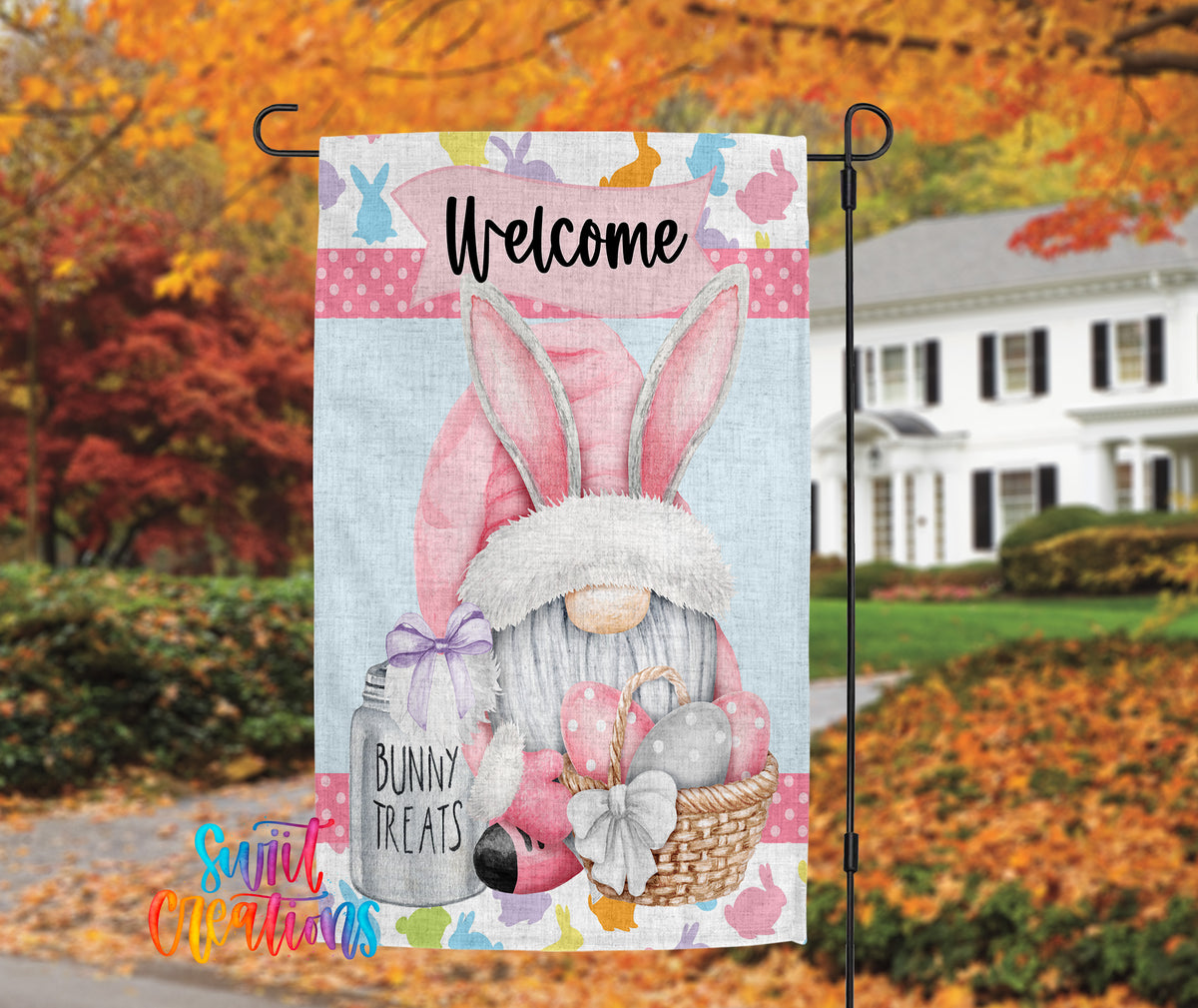 A colorful welcome sign featuring a bunny gnome holding a basket of Easter eggs and treats, with a house and autumn trees in the background.