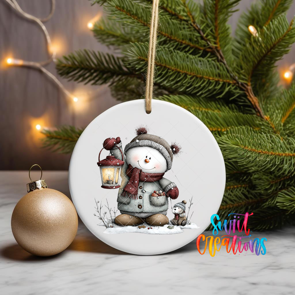 A white ceramic ornament featuring a snowman holding a lantern, surrounded by a Christmas tree and a gold ornament, with a text overlay that reads "Sweet Creations".