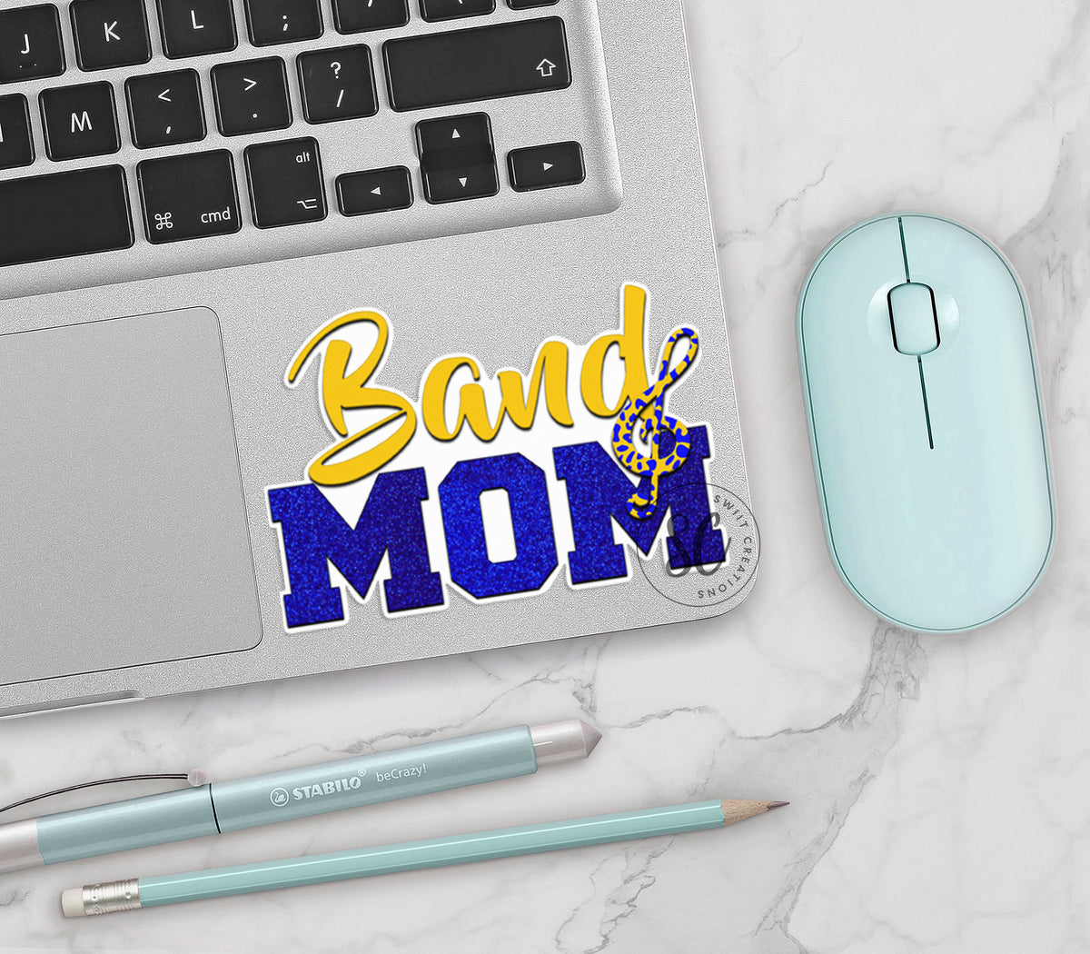 Gold and Blue Band Mom vinyl sticker on a silver laptop next to a mint mouse and pens