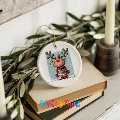 A ceramic ornament featuring a cartoon reindeer is displayed on top of a stack of books, surrounded by greenery.