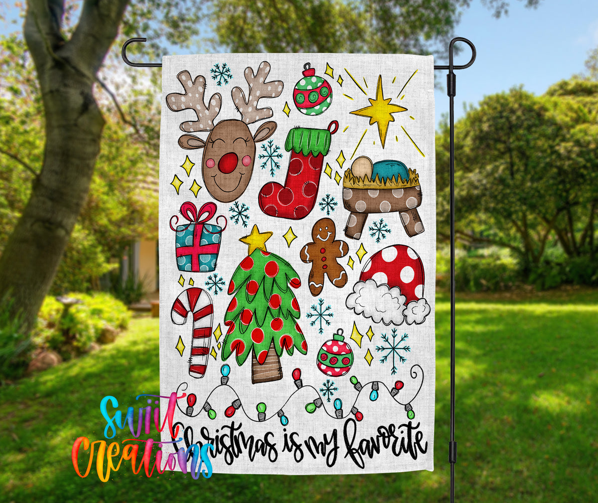 A colorful Christmas-themed flag with various holiday-related icons and decorations, including a reindeer, Christmas tree, gingerbread man, nativity scene, and other festive elements, all set against a natural outdoor backdrop.