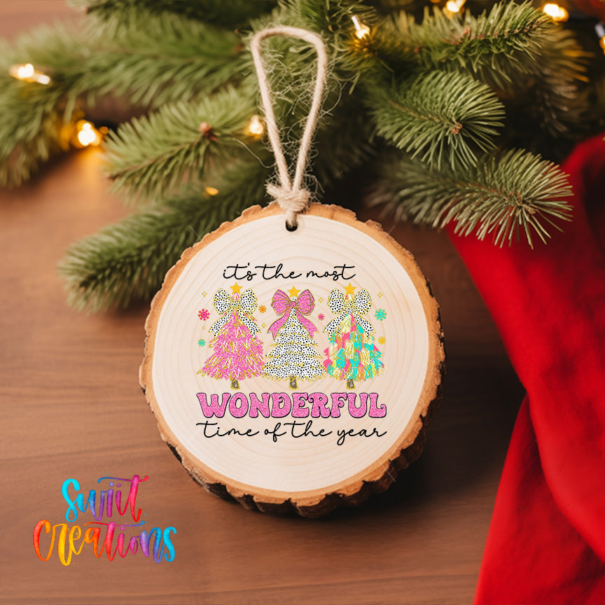 A wooden ornament with a festive design hangs on a Christmas tree, surrounded by greenery and twinkling lights.