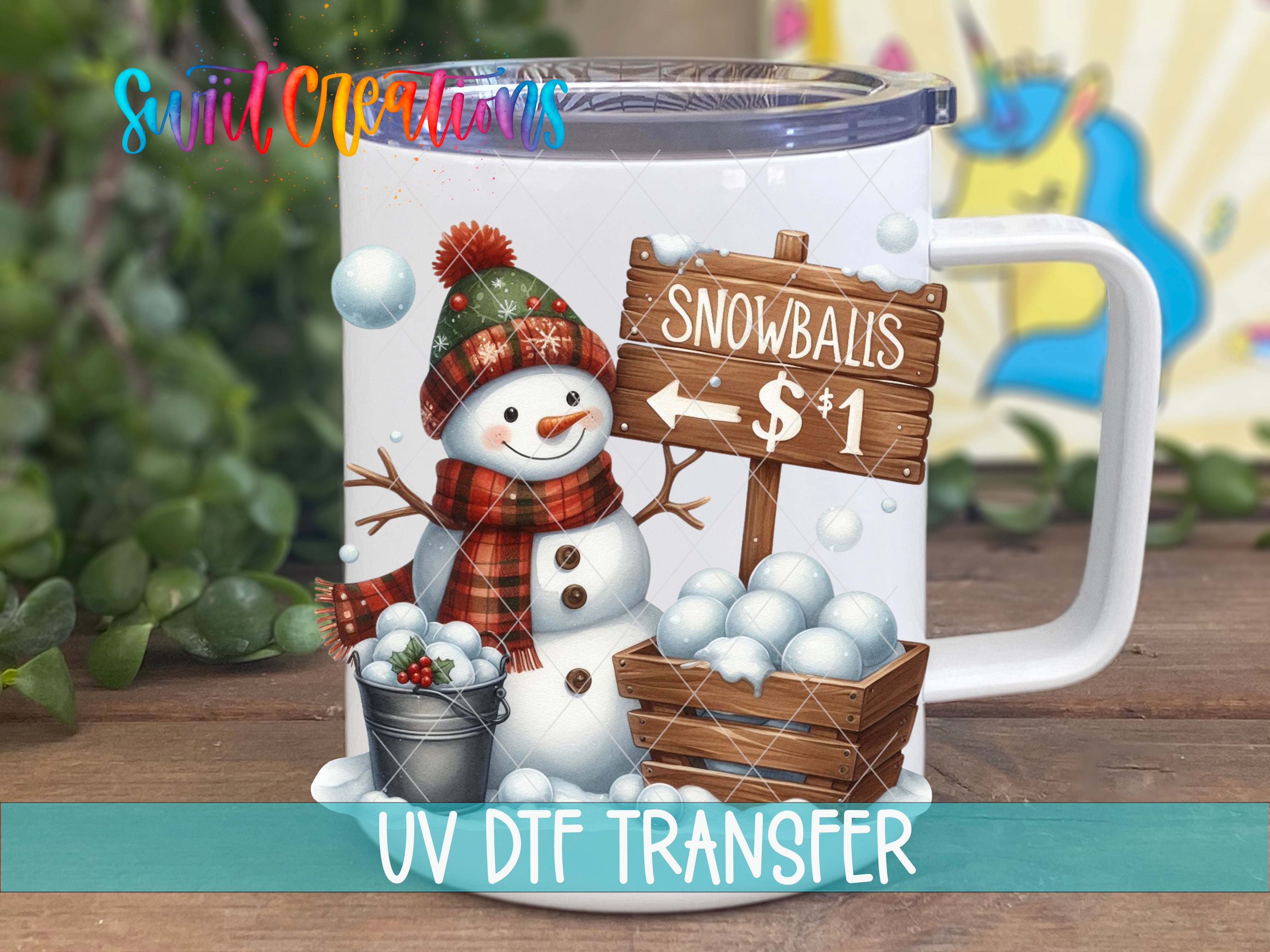 A mug with a snowman and snowballs on it, along with a sign that says "Snowballs $1". The mug is placed on a wooden surface, and there is a blurred background that appears to be a garden or snowy landscape.