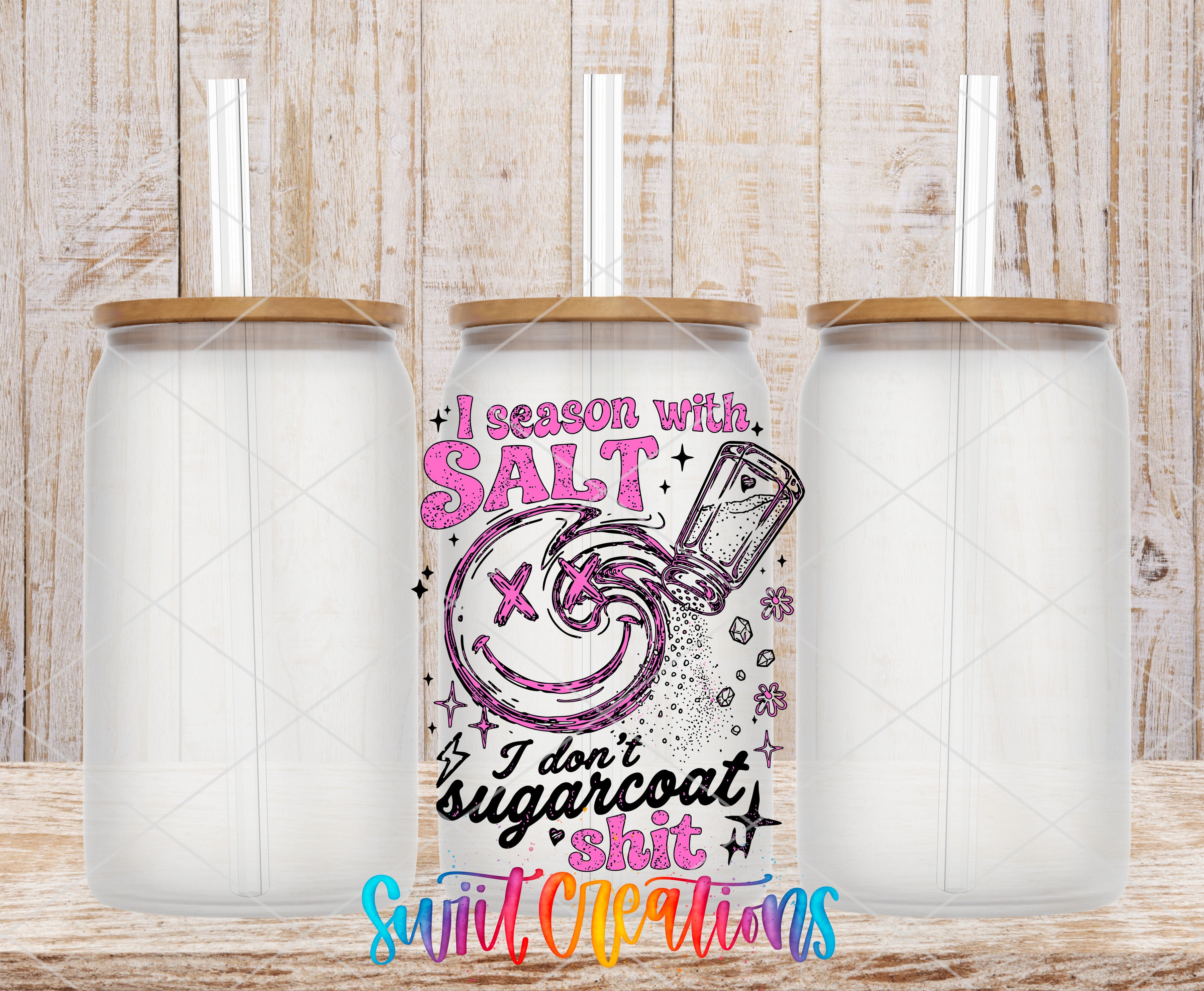 three clear glass jars with wooden lids, arranged in a row against a wooden background. The jars appear to be empty, and there is a colorful graphic design or text on the jars that reads "I season with salt" and "I don't sugarcoat it".