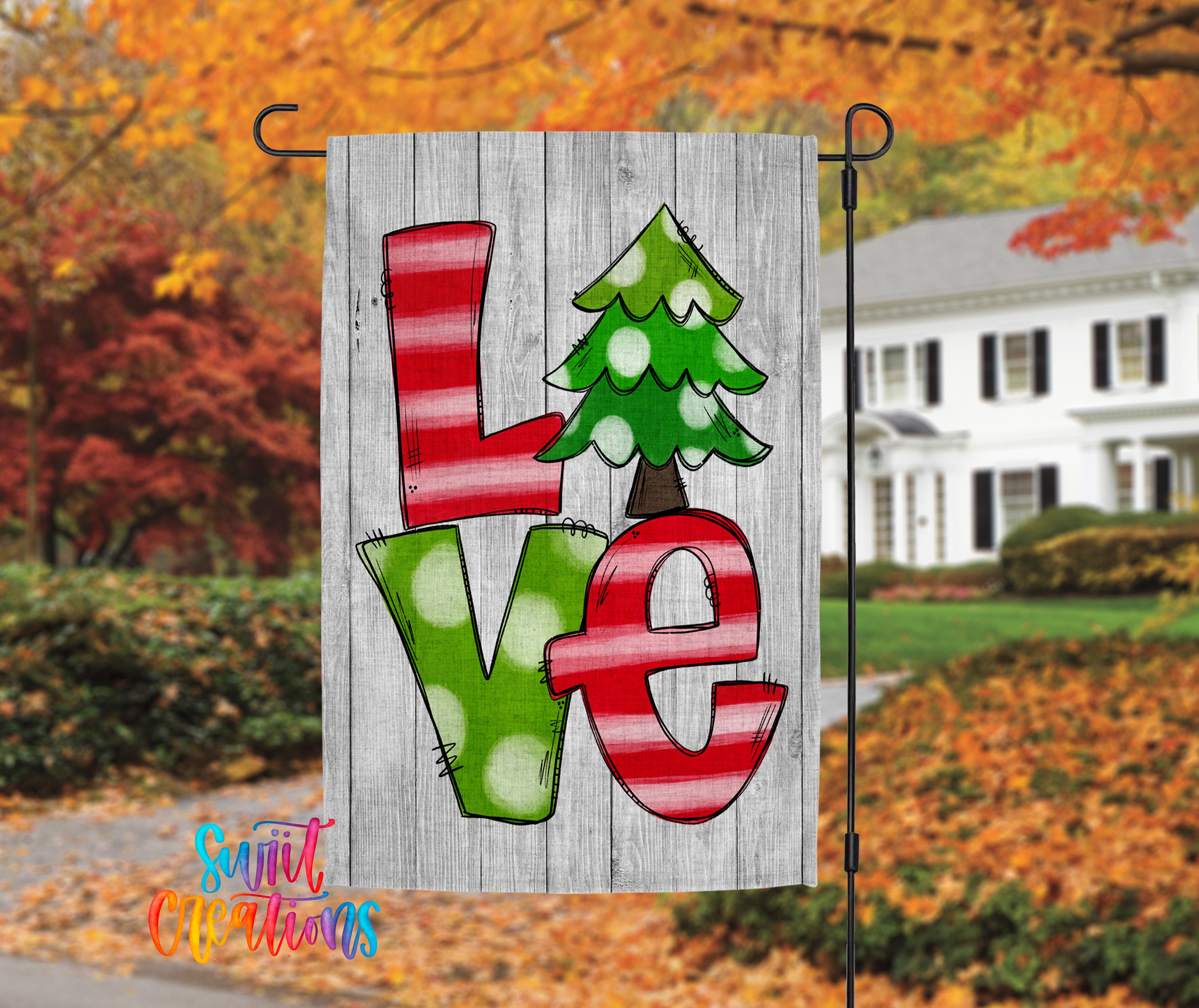 A wooden flag with a colorful design hanging in front of a house with autumn trees in the background.