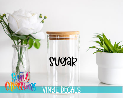 a clear glass jar with a wooden lid, a white vase with white flowers, and a potted plant, all placed on a white surface.