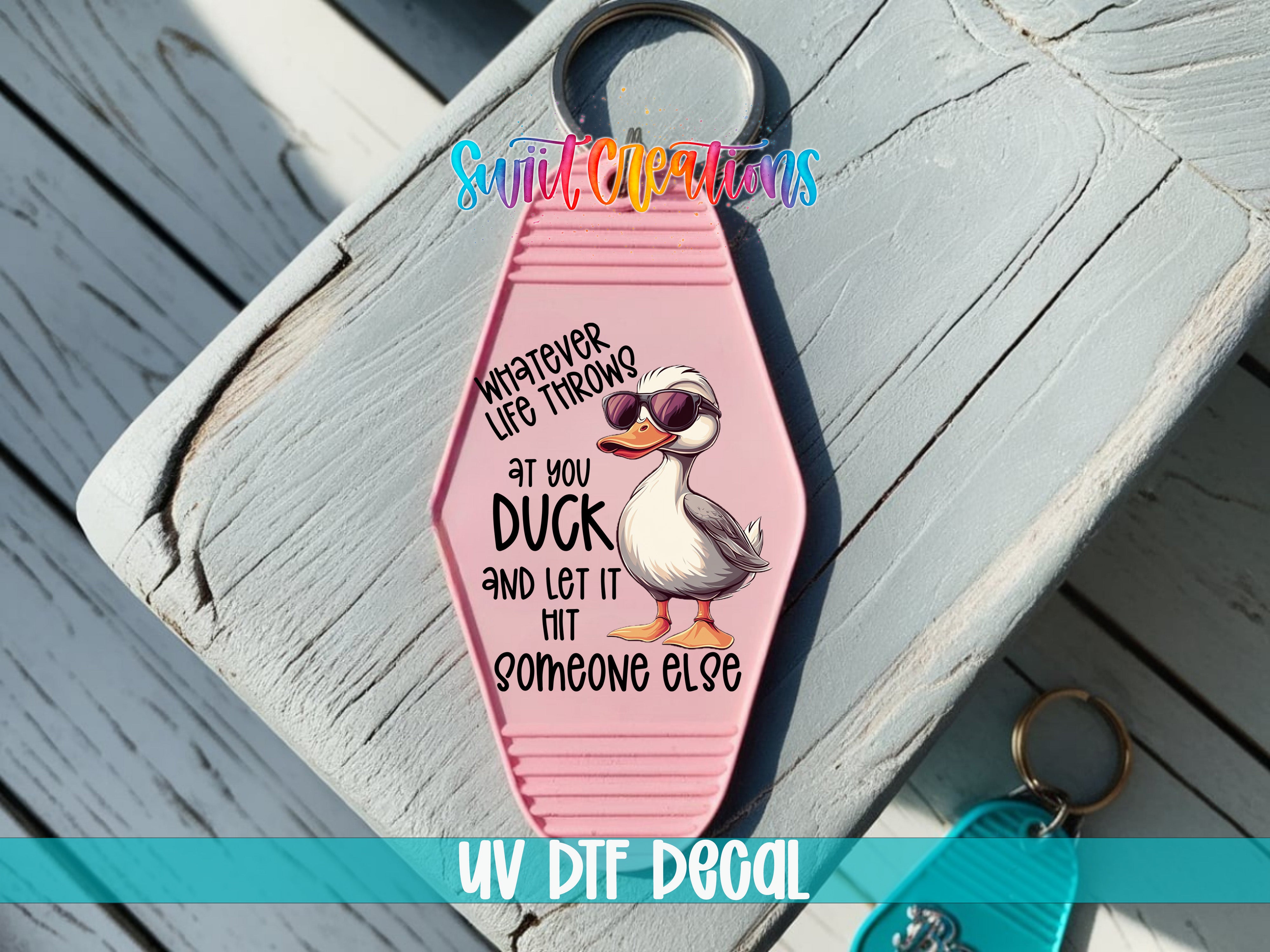 A pink keychain with a cartoon duck and text on it, placed on a wooden surface.