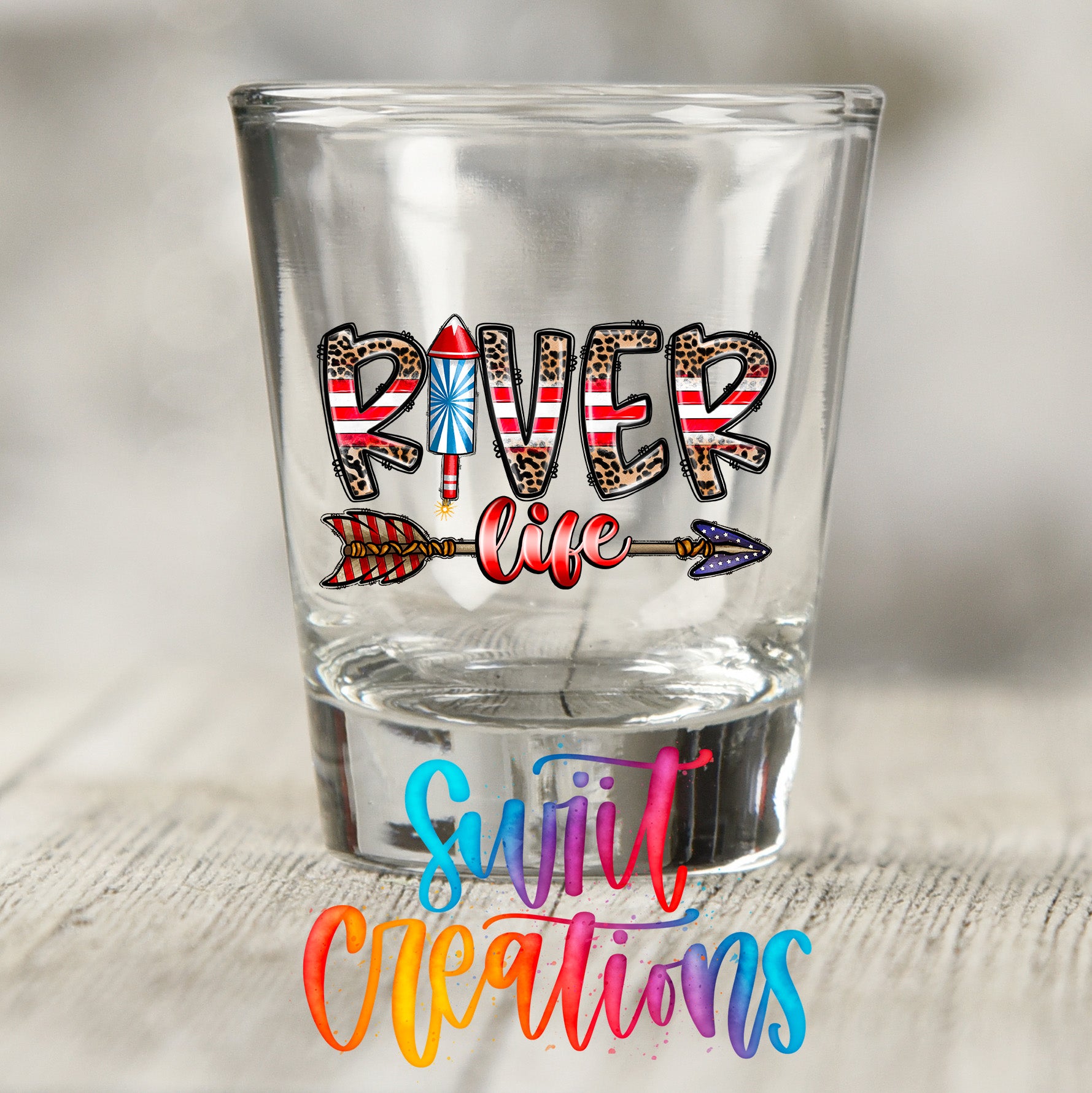 A shot glass with the word "RIVER" printed on it, along with an arrow and fireworks-like designs.