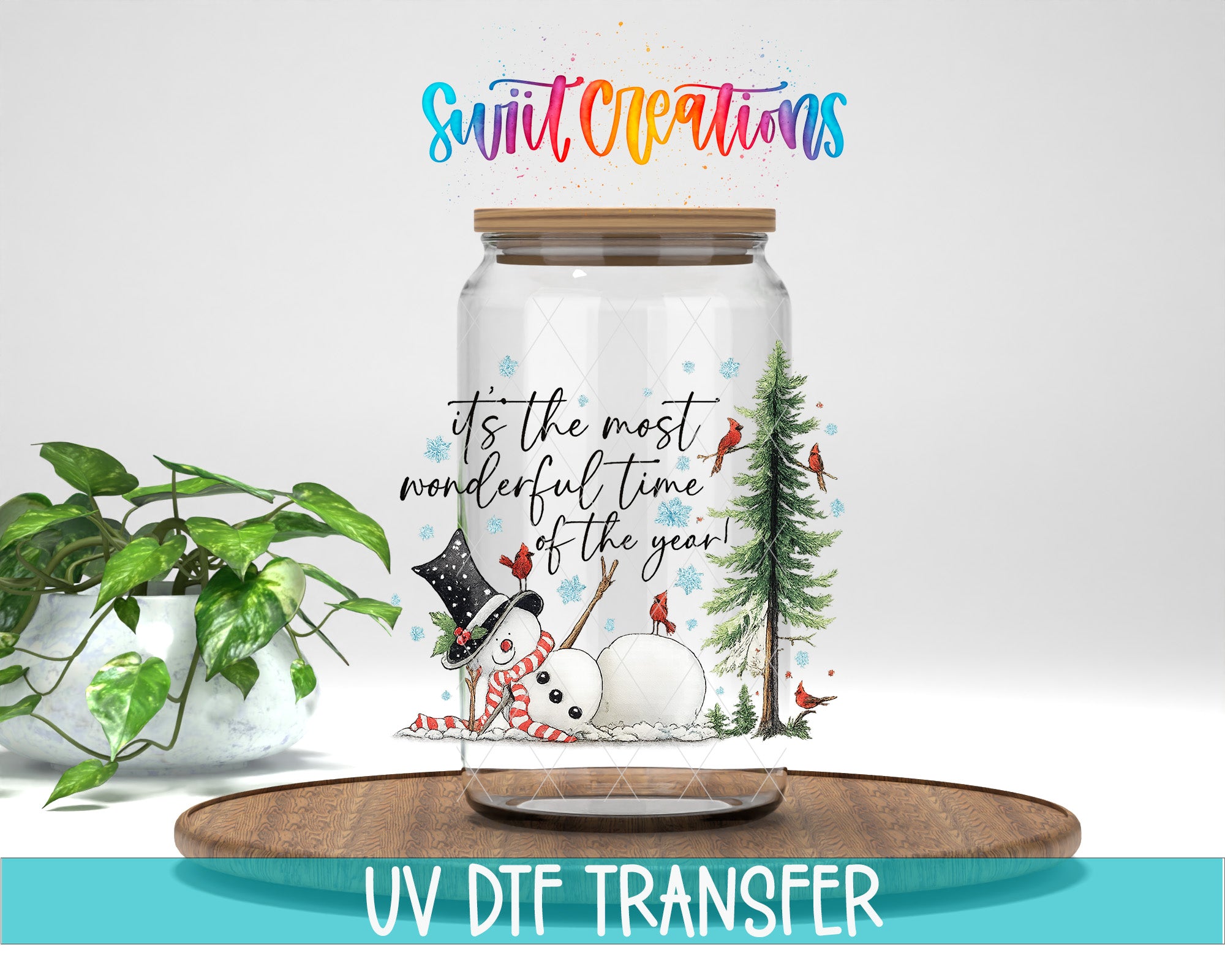 A glass jar with a snowman and pine tree design, along with the text "It's the most wonderful time of the year!" and a colorful logo. The jar is placed on a wooden tray, and there is a potted plant in the background.