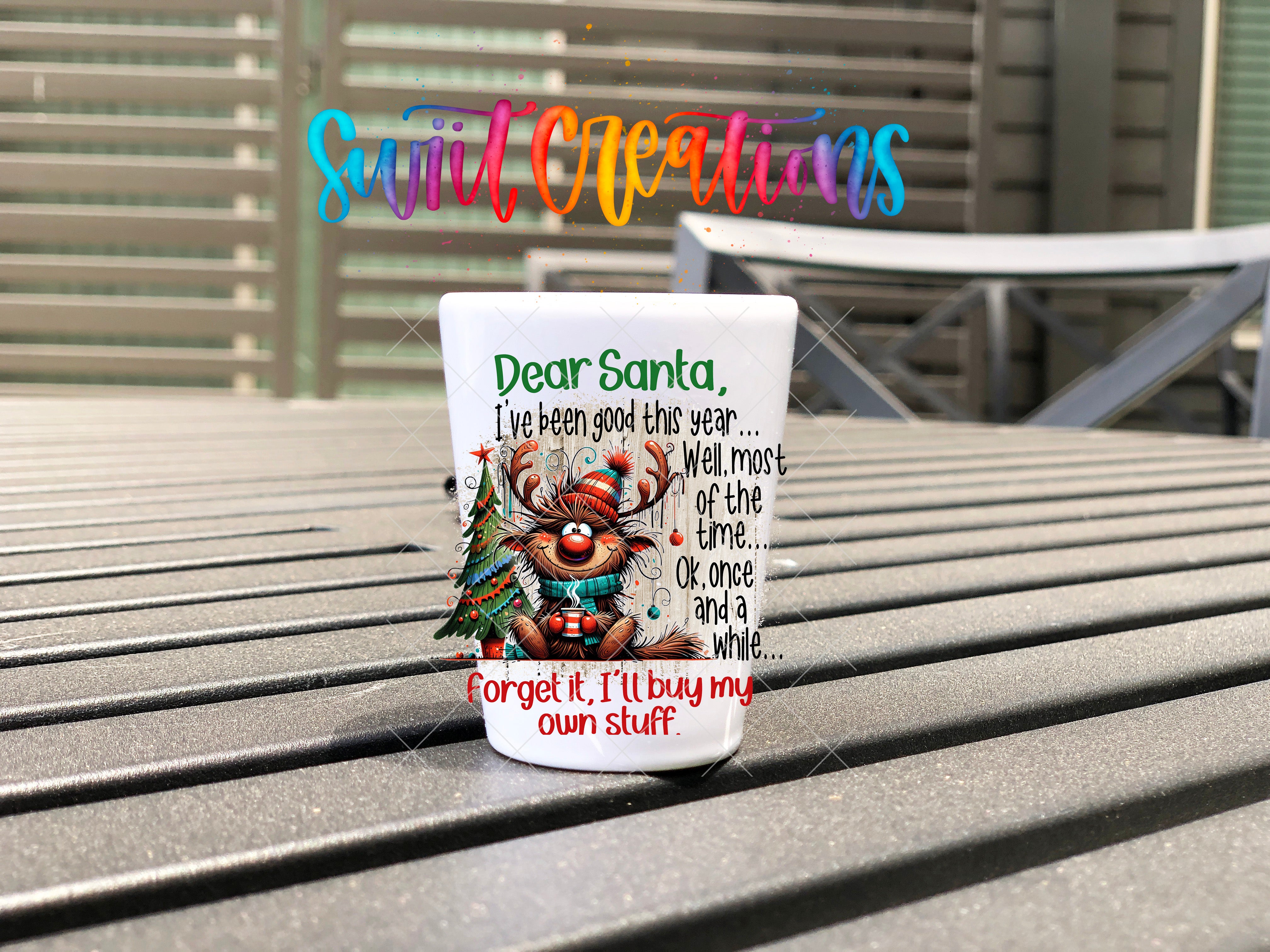 A mug with a Christmas-themed design featuring a reindeer and text that says "Dear Santa, I've been good this year... Well most of the time... Ok, once and a while and a while..." The mug is placed on a wooden surface, and there is a colorful text overlay in the background that says "Swift Creations".