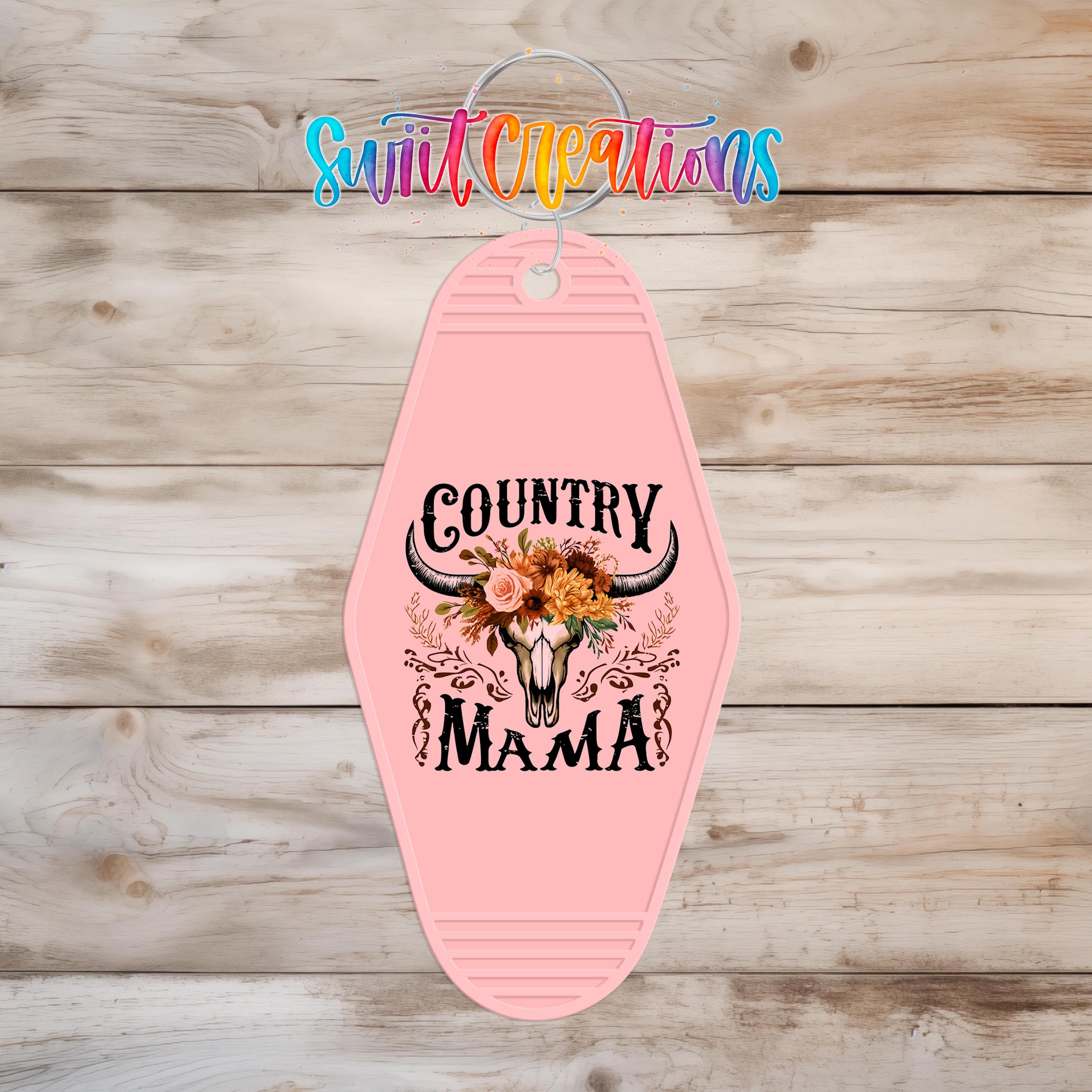 A pink keychain with a design featuring a skull and floral elements, along with the text "Country Mama".
